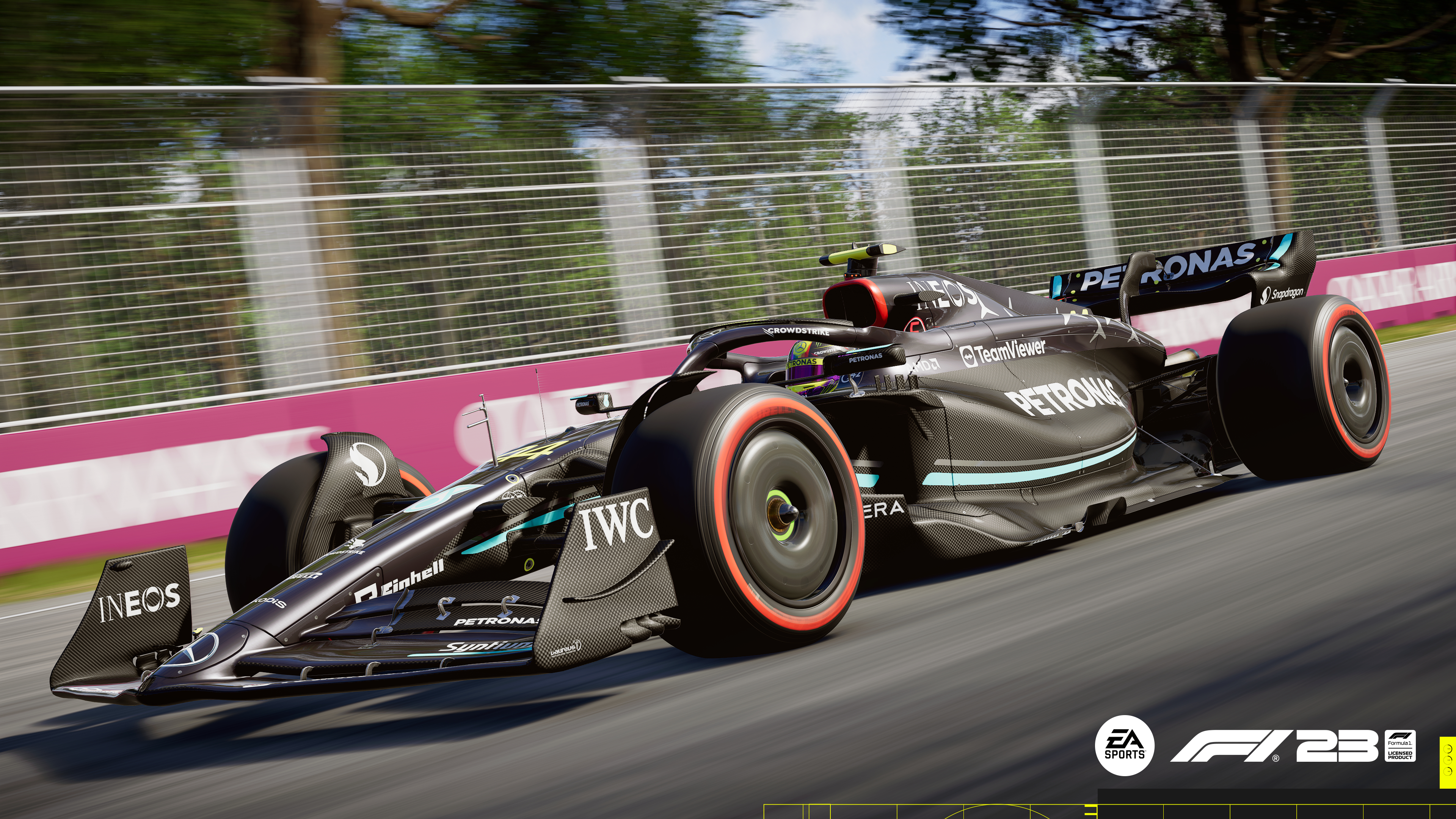 F1-Rennwagen auf der Strecke, schwarz und weiß. Sponsorenlogos sichtbar. Bäume und Barrieren im Hintergrund.