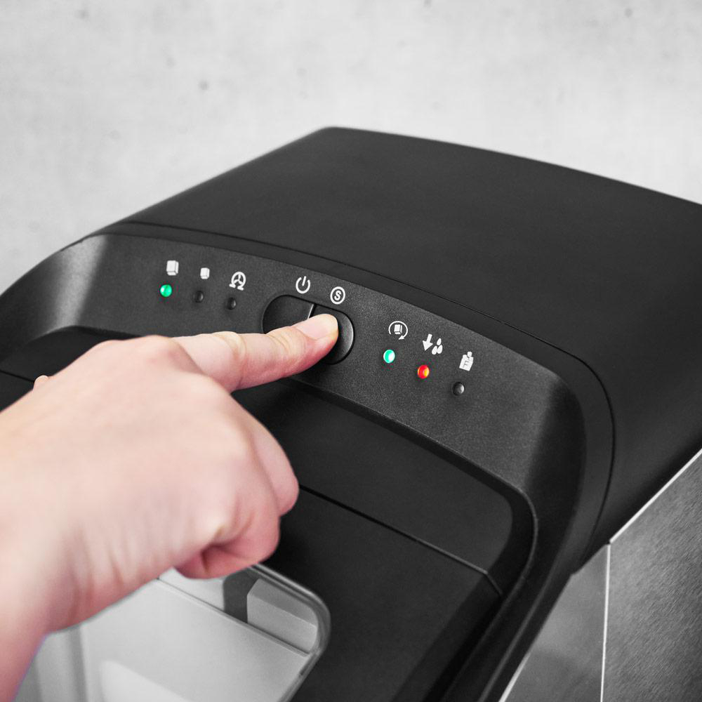 Eine Hand drückt eine Taste auf einem schwarzen Gerät mit grünen und roten Kontrollleuchten.