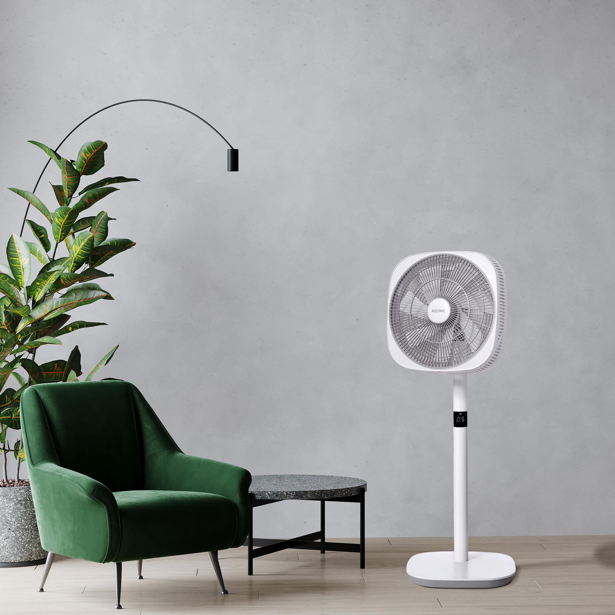 Ein Wohnzimmer mit einem grünen Sessel, einem weißen Ventilator und einer Pflanze neben einer grauen Wand.