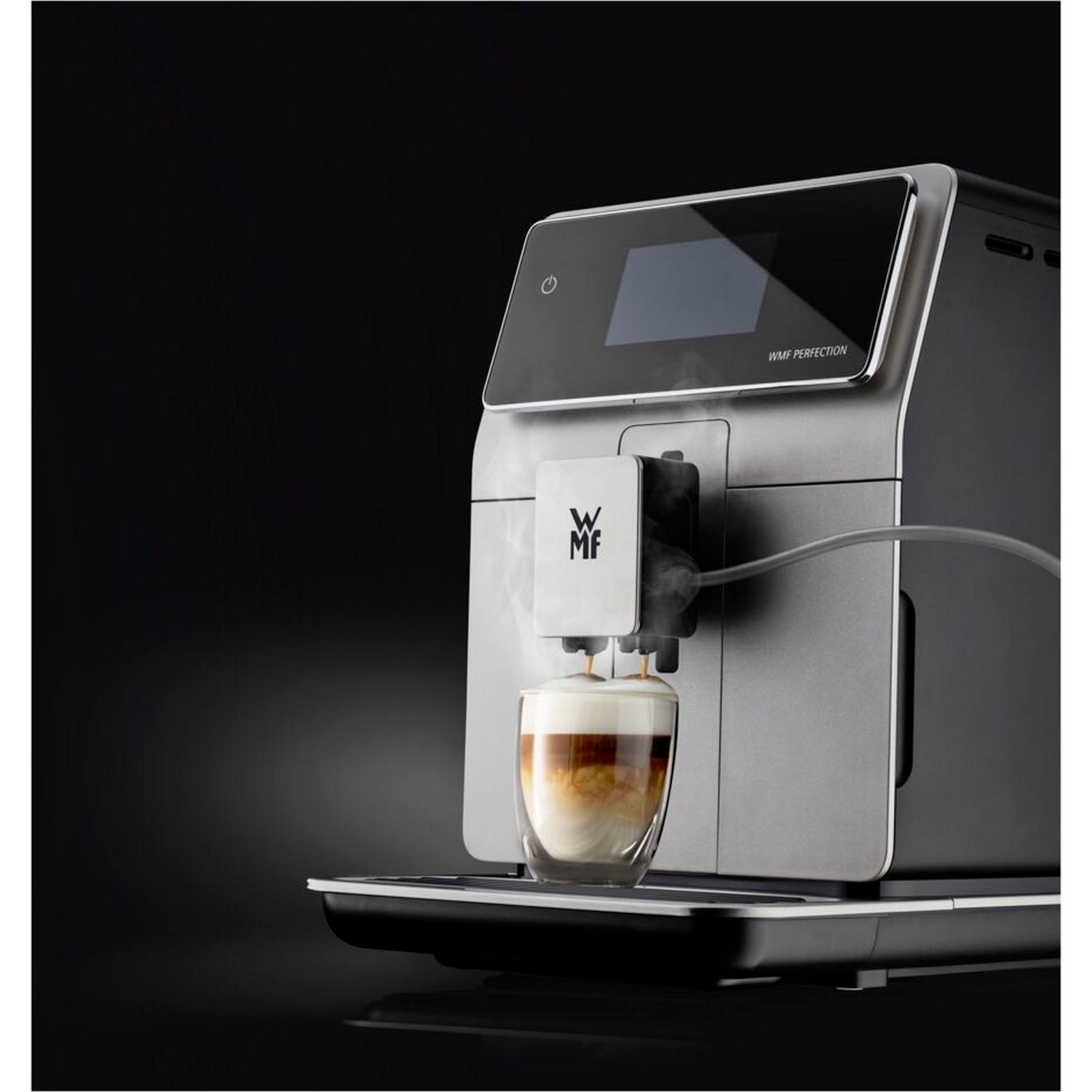 Silver and black coffee machine, with a coffee cup, steam coming out, on a black background.