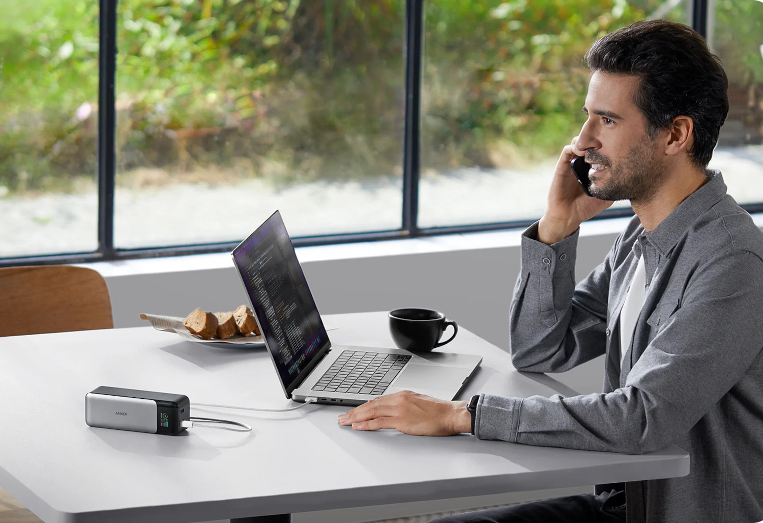 A man on the phone at a table with a laptop and a charger.