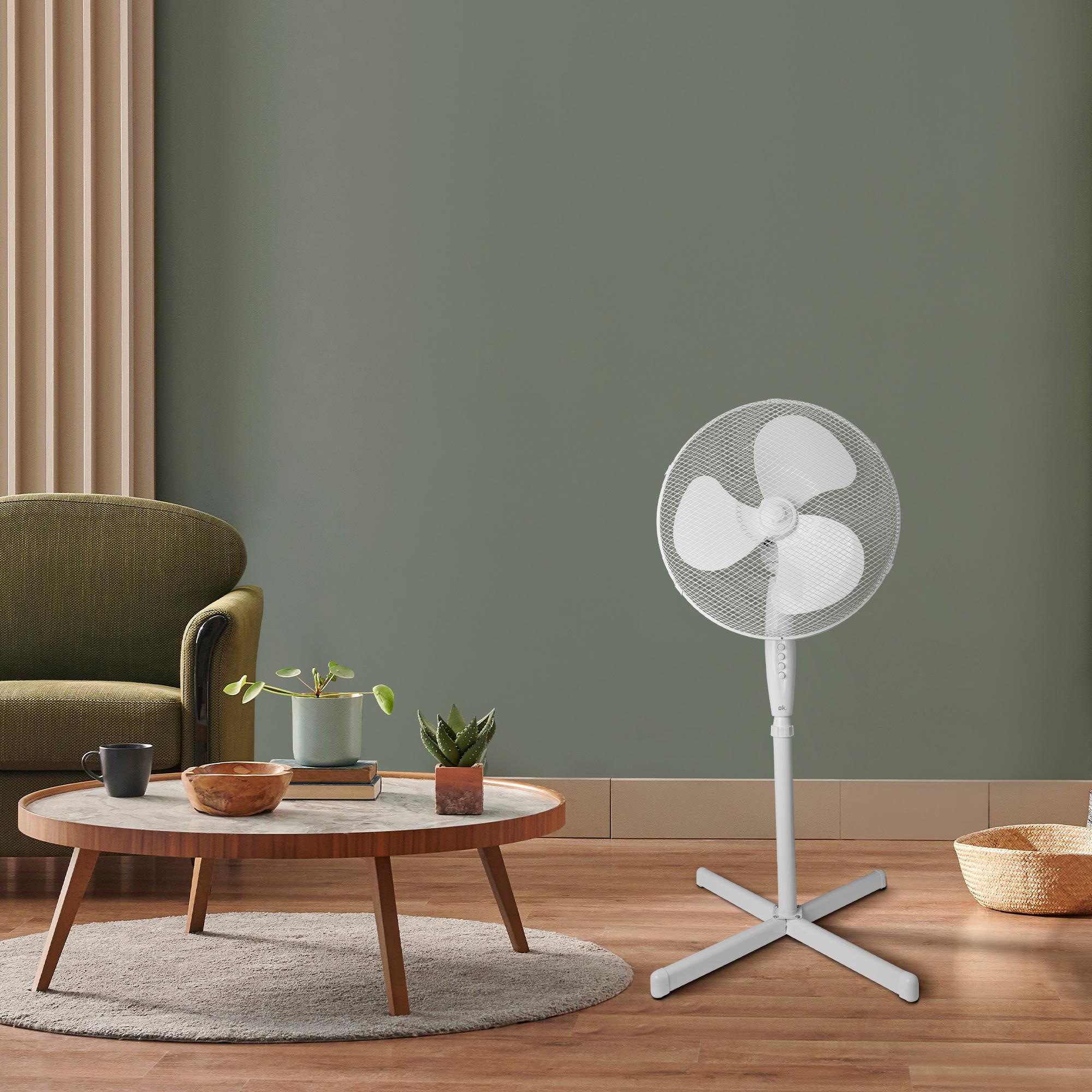 Weißer Ventilator in einem Wohnzimmer. Er steht vor einer grünen Wand mit Möbeln.