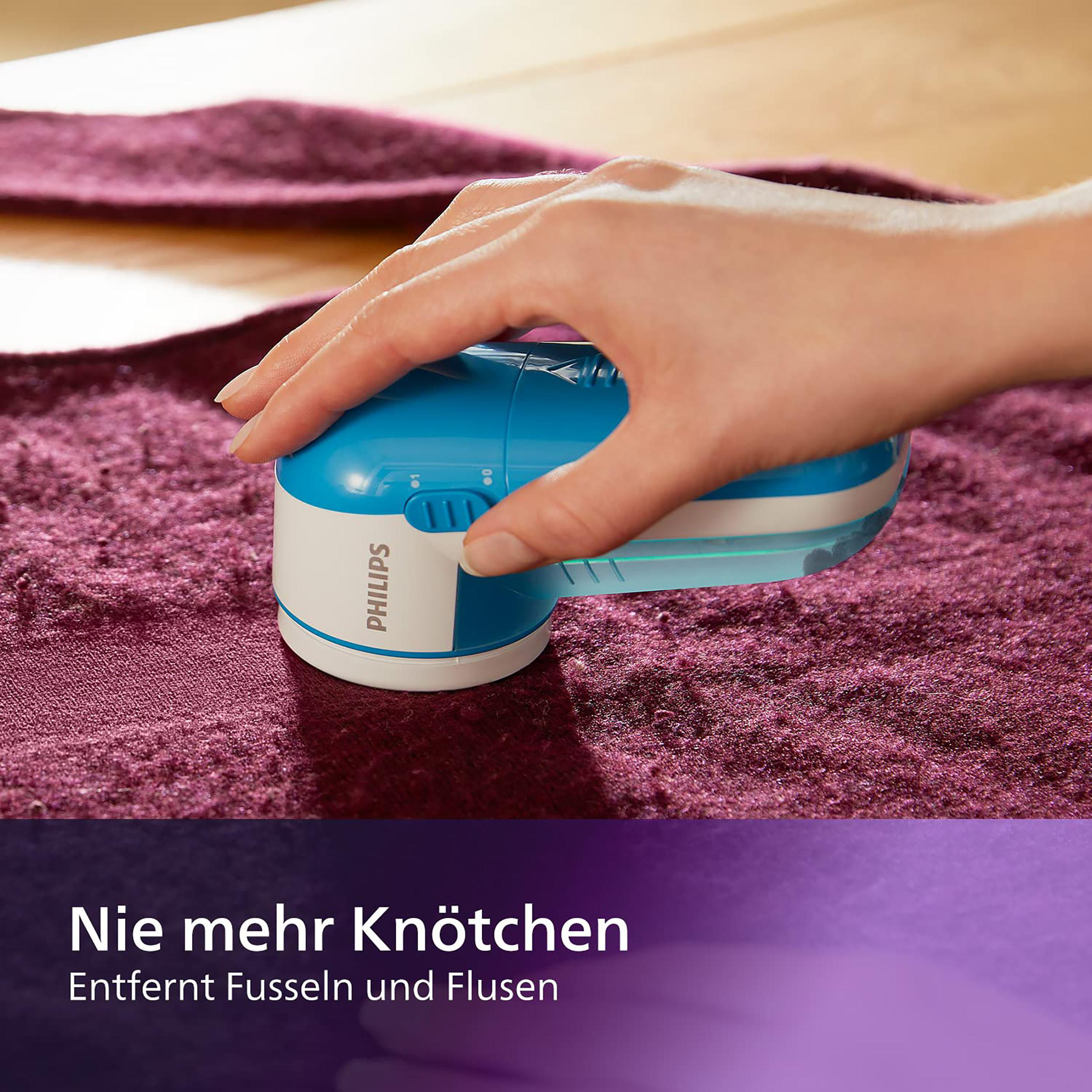 Hand benutzt blauen/weißen Fusselrasierer auf lila Oberfläche.