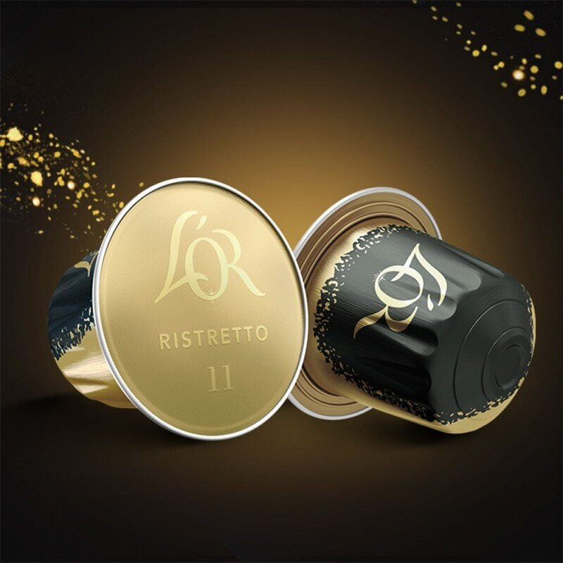 Dwie kapsułki kawy, jedna otwarta. Kolory złoty i czarny. Marka L'OR Ristretto. Ciemne tło ze złotymi iskierkami.