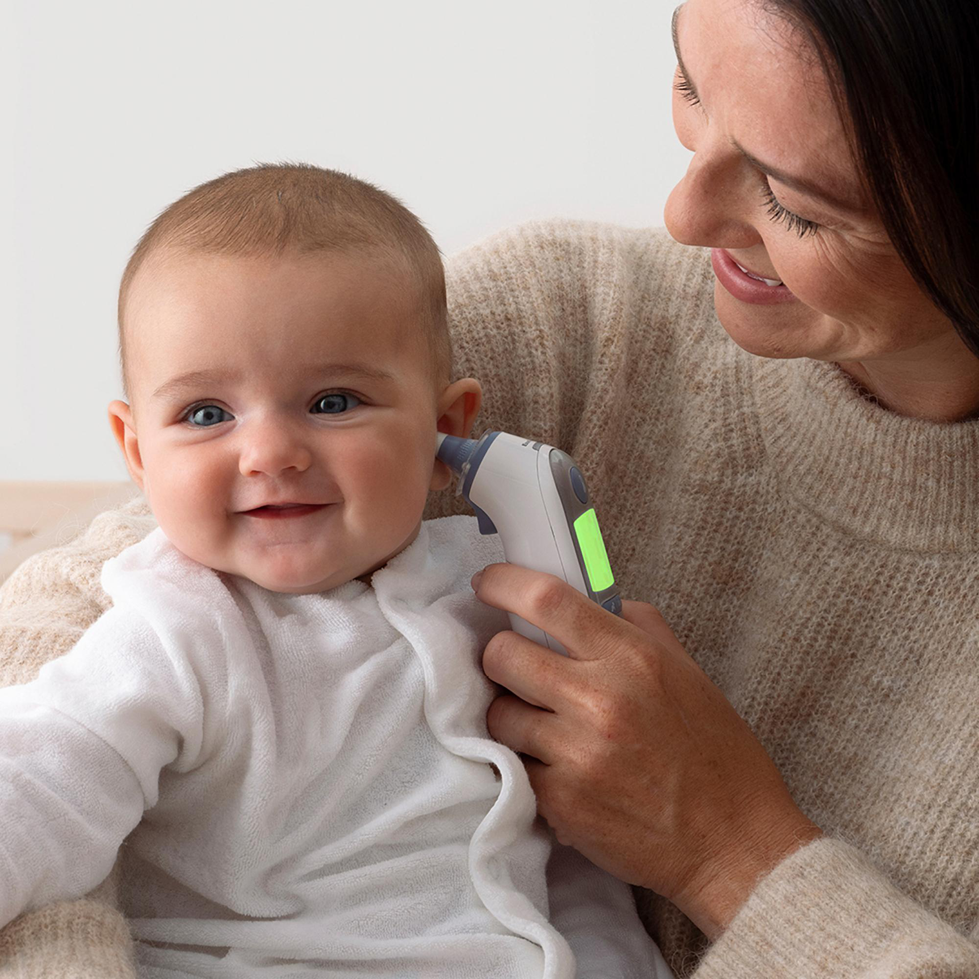 Eine Frau misst die Temperatur eines Babys mit einem digitalen Thermometer. Beide lächeln.