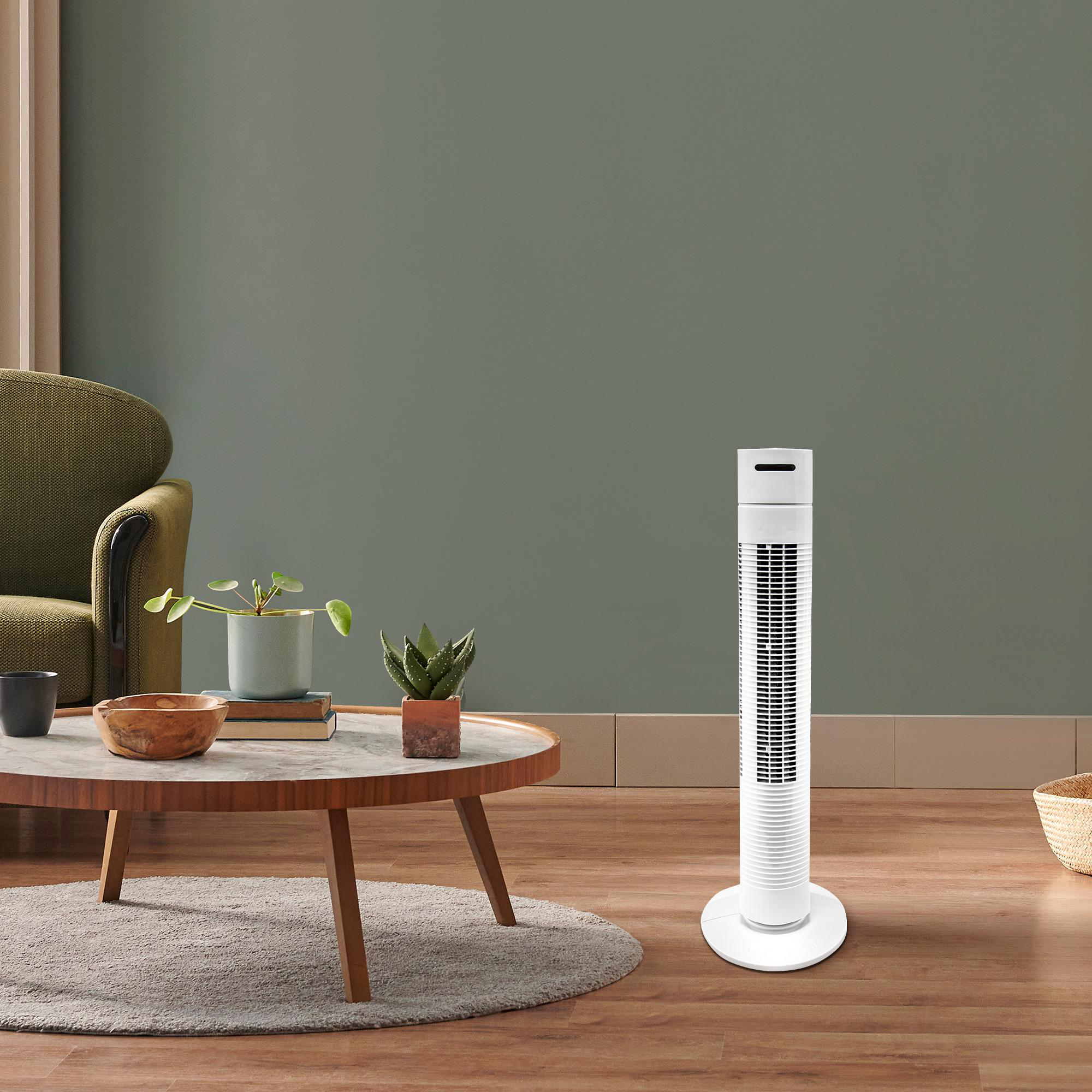 Weißer Turmventilator in einem Wohnzimmer. Der Ventilator steht auf einem Holzboden. Grüner Hintergrund.