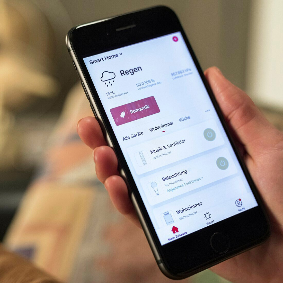 Ręka osoby trzymająca smartfona z interfejsem aplikacji inteligentnego domu. Telefon jest czarny.