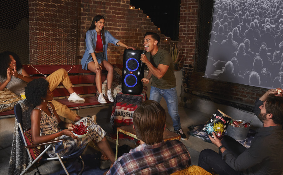 Grupo de personas al aire libre, cantando y disfrutando de una sesión de karaoke con un altavoz.