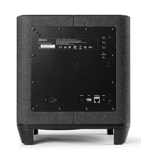 Tył szarego subwoofera Denon. Ma czarny panel z portami i połączeniem zasilania.