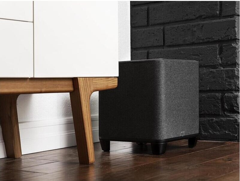 Czarny subwoofer obok białej szafki i ceglanej ściany.