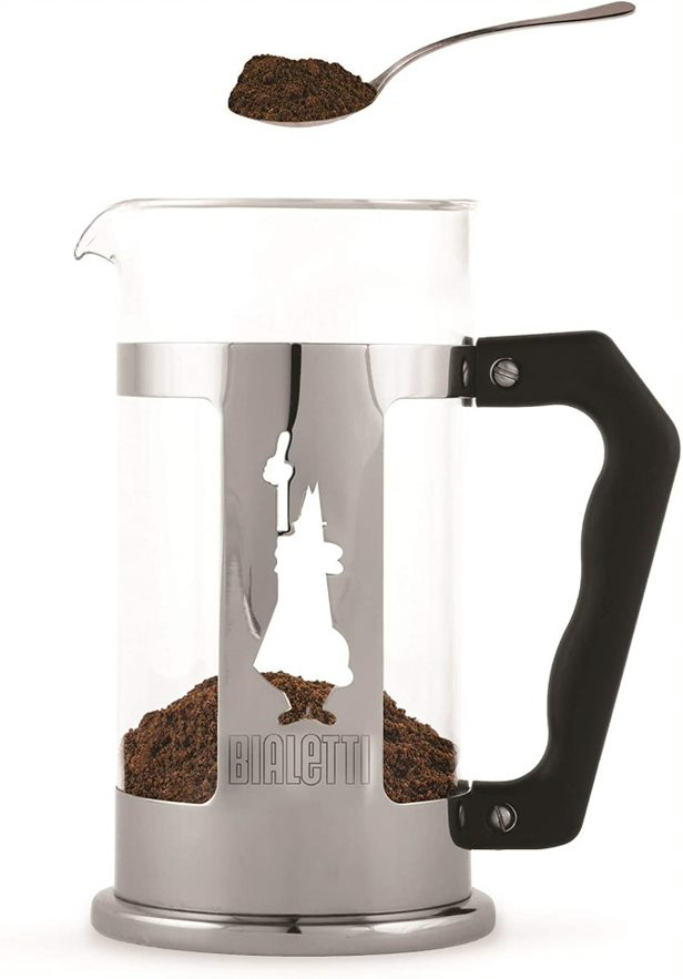 Üveg french press őrölt kávéval, tetején egy kávéval teli kanállal.