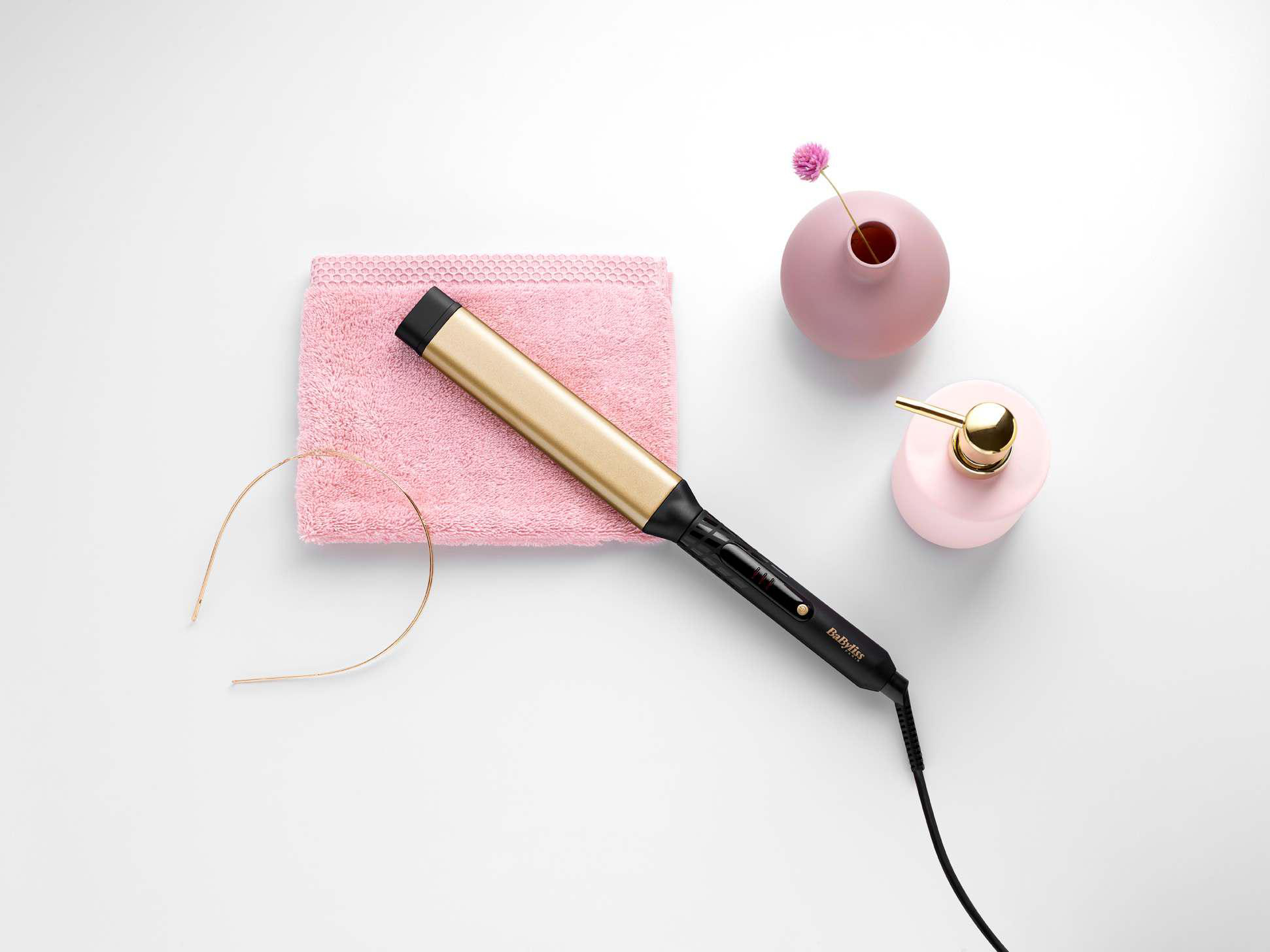 Haarstyling-Set: Lockenstab, rosa Handtuch, Haarreif, rosa Vase mit Blume.