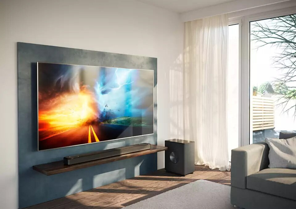 Telewizor zamontowany na ścianie, soundbar poniżej. Pokój z oknem, sofą. Burzowe niebo na ekranie.
