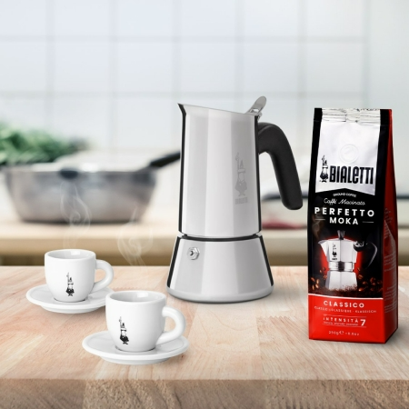 Kávékészlet egy Bialetti Mokával, két csészével, csészealjjal és egy zacskó kávébabbal.