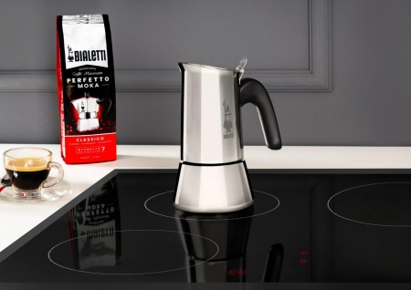 Egy rozsdamentes acél Bialetti Moka a fekete indukciós főzőlapon, egy kávézacskóval a közelben.