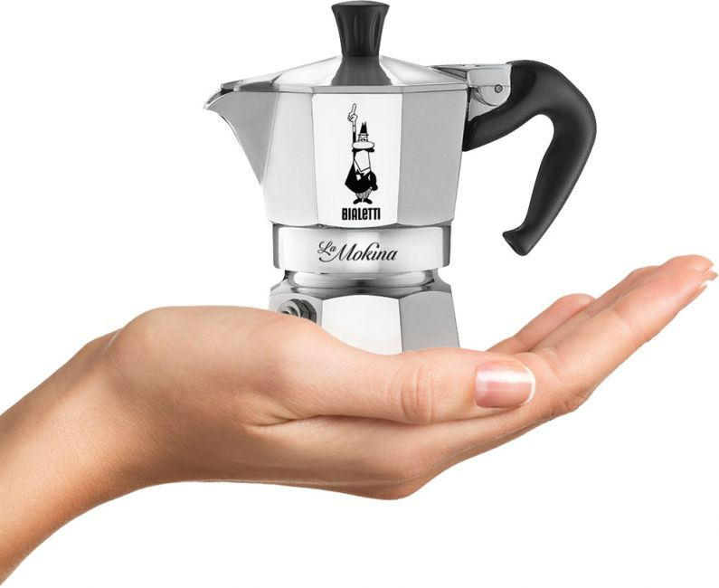 Egy kéz egy ezüst-fekete Moka kávéfőzőt tart. A kávéfőző fekete fogantyúval és Bialetti logóval rendelkezik.
