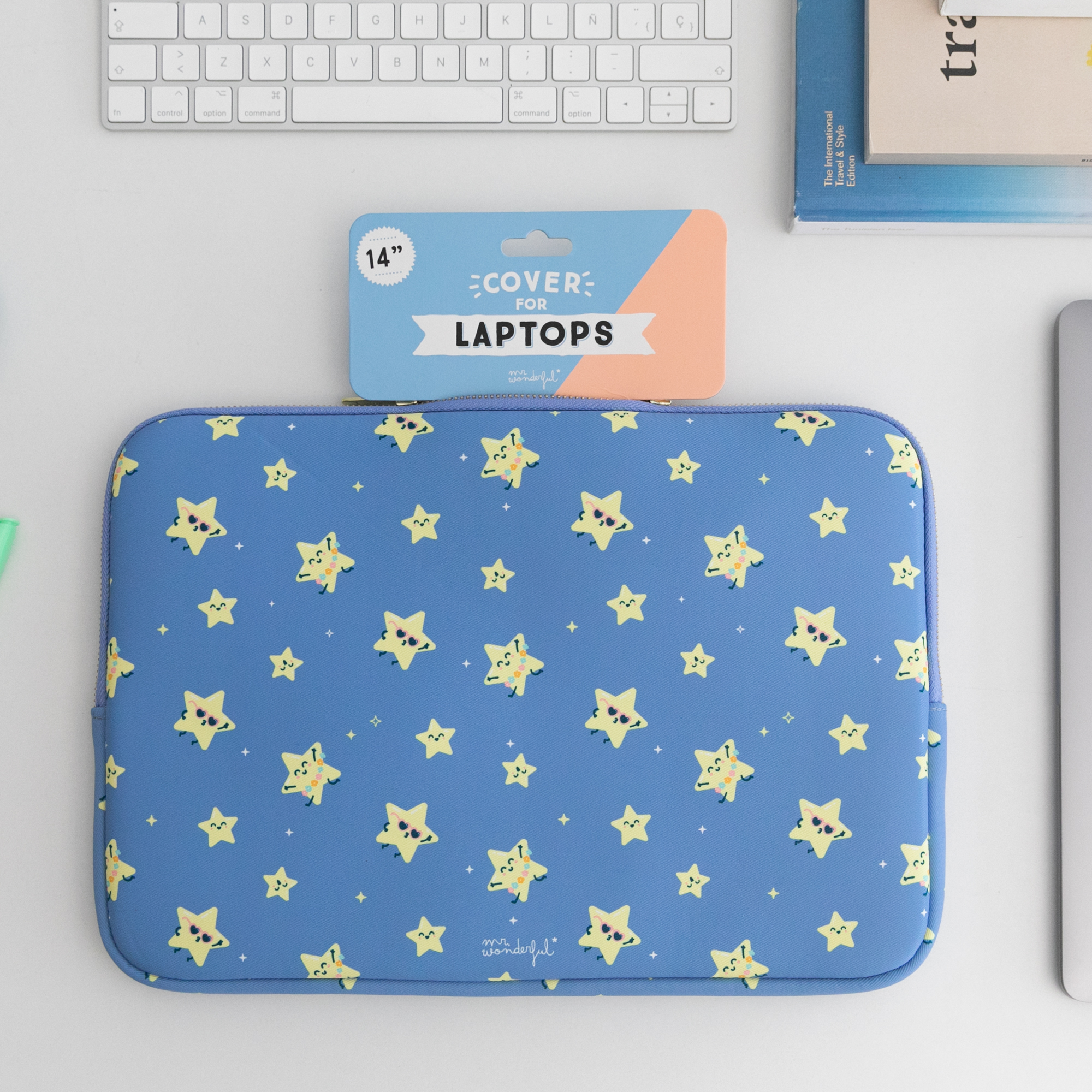 Una funda azul para portátil con un patrón de estrellas. Un teclado y un portátil están sobre la superficie blanca.