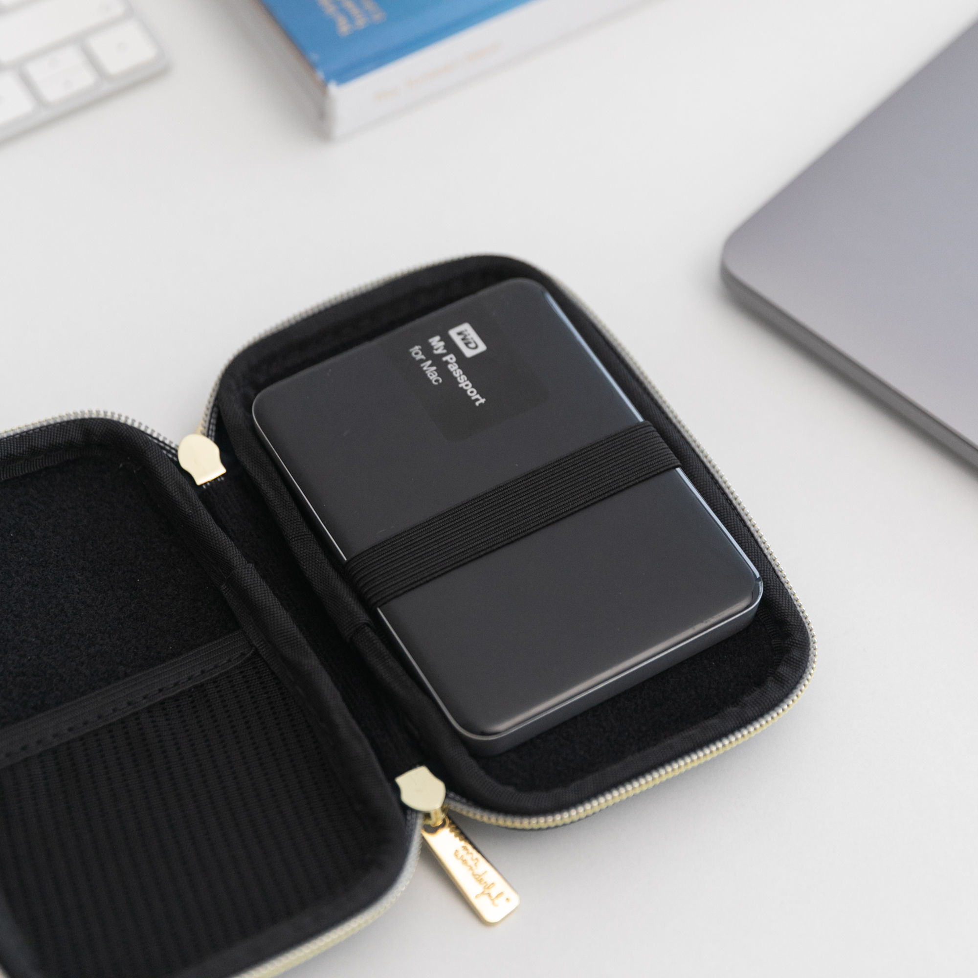 Disco duro externo dentro de una funda con cremallera, junto a un portátil y otros objetos.