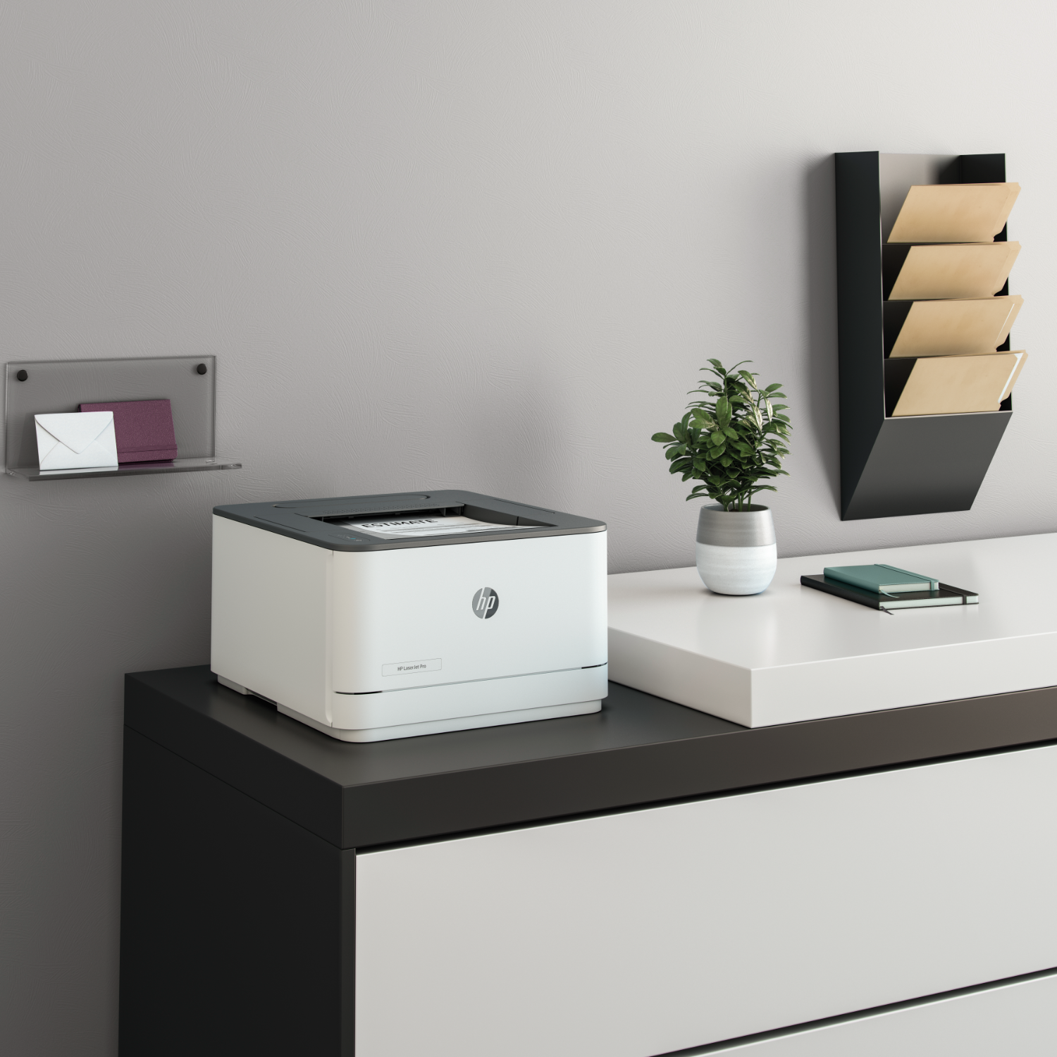 A printer on a white and black desk with a plant and a file organizer in the background.