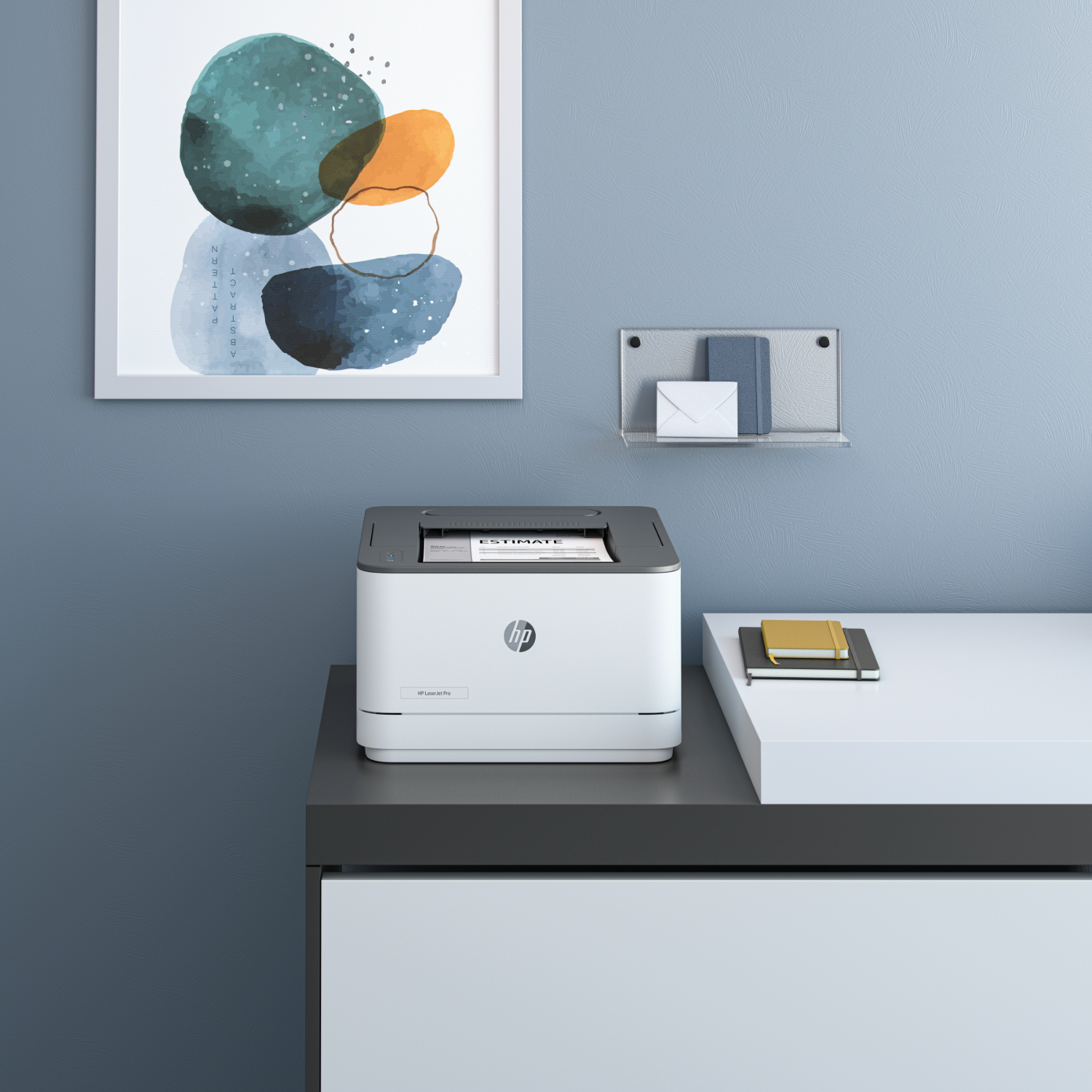 A printer on a desk with a picture and a notebook. The wall is blue. The desk and drawers are in black and white.