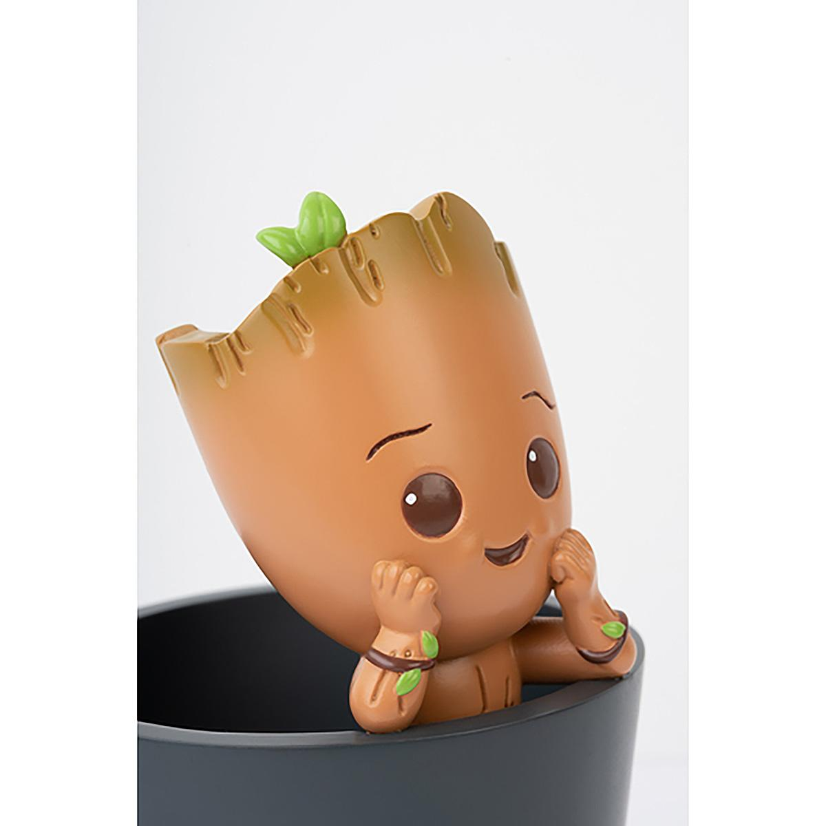 Niedliche Groot-Figur in einem dunklen Topf, Kopf geneigt. Grüne Blätter und Details sichtbar.