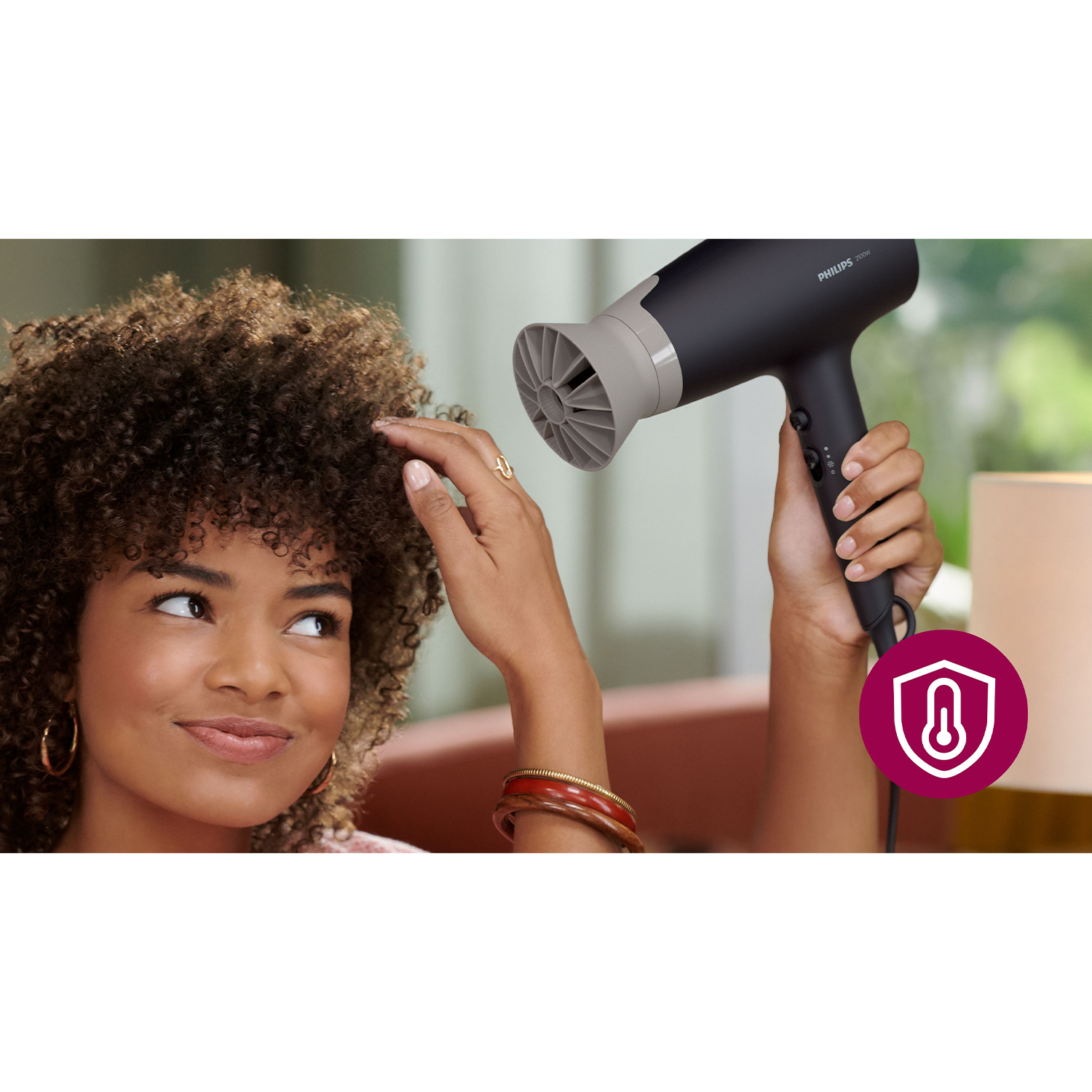 Donna con capelli ricci usa un asciugacapelli nero e grigio. Icona di protezione termica visibile.