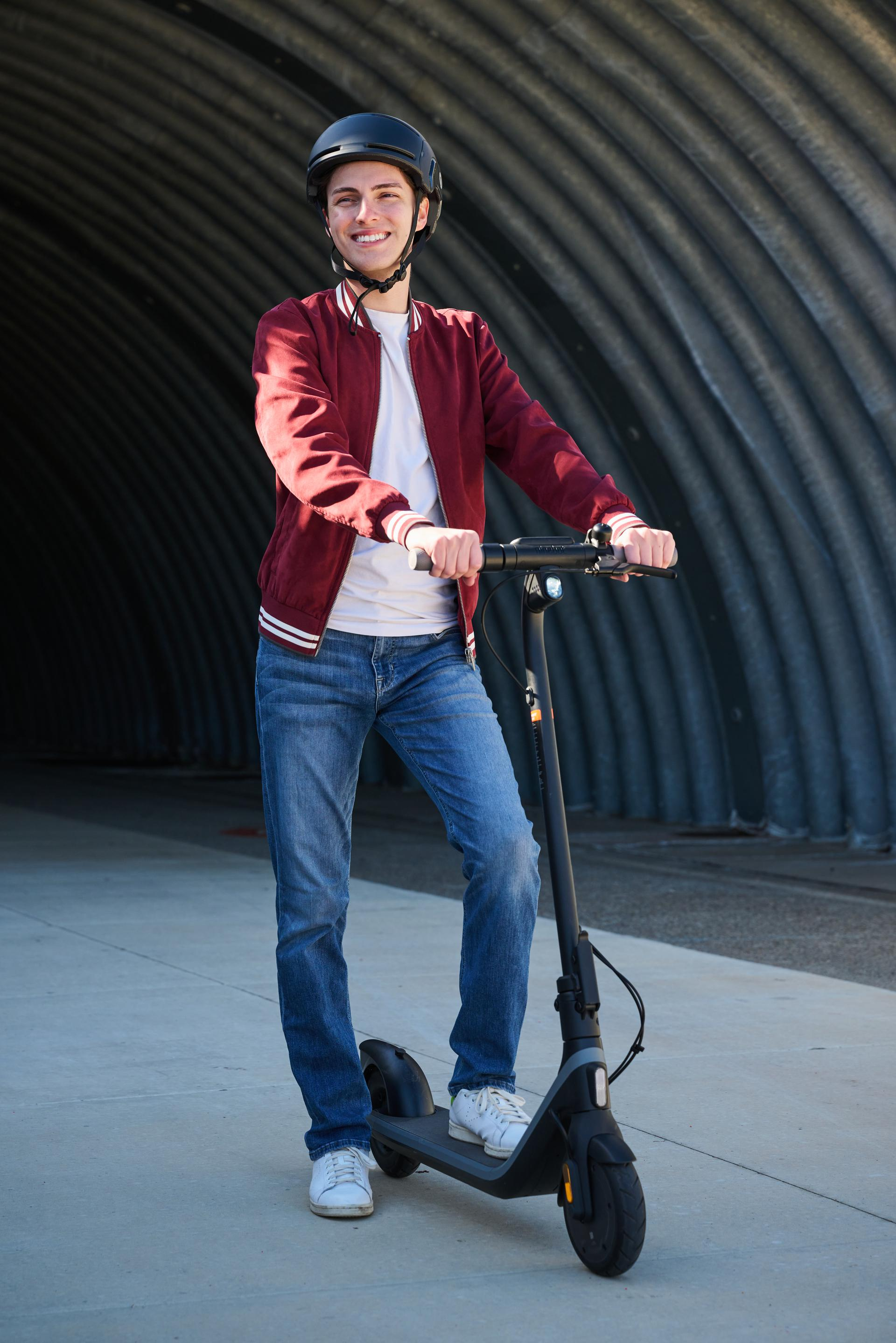Joven con casco y vaqueros, de pie en un patinete en un túnel.