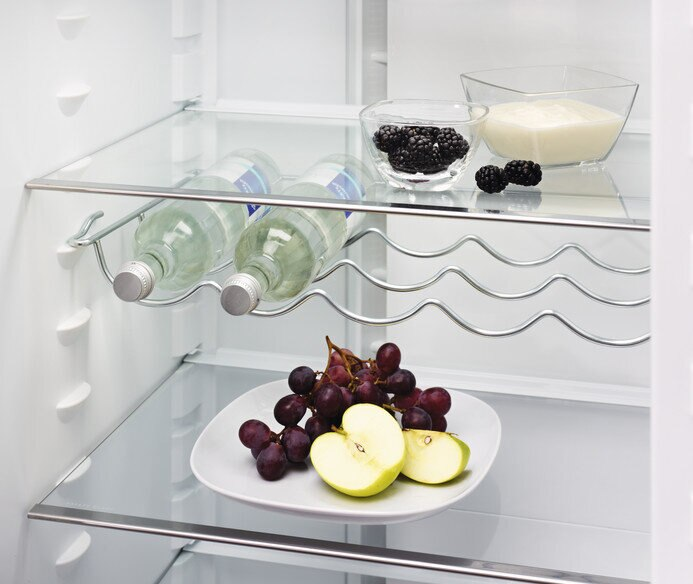 Półka w lodówce z butelkami, winogronami i talerzem z plasterkami jabłka.