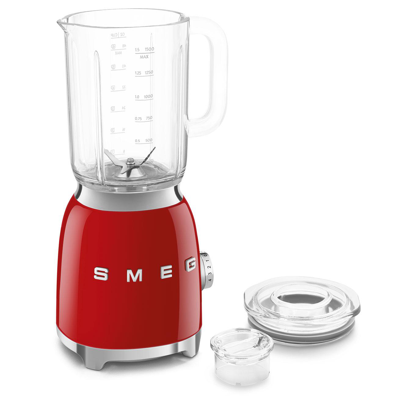 Ein roter Smeg-Mixer mit einem Glasbehälter und Deckel. Ein kleiner Deckel und Becher daneben. Weißer Hintergrund.
