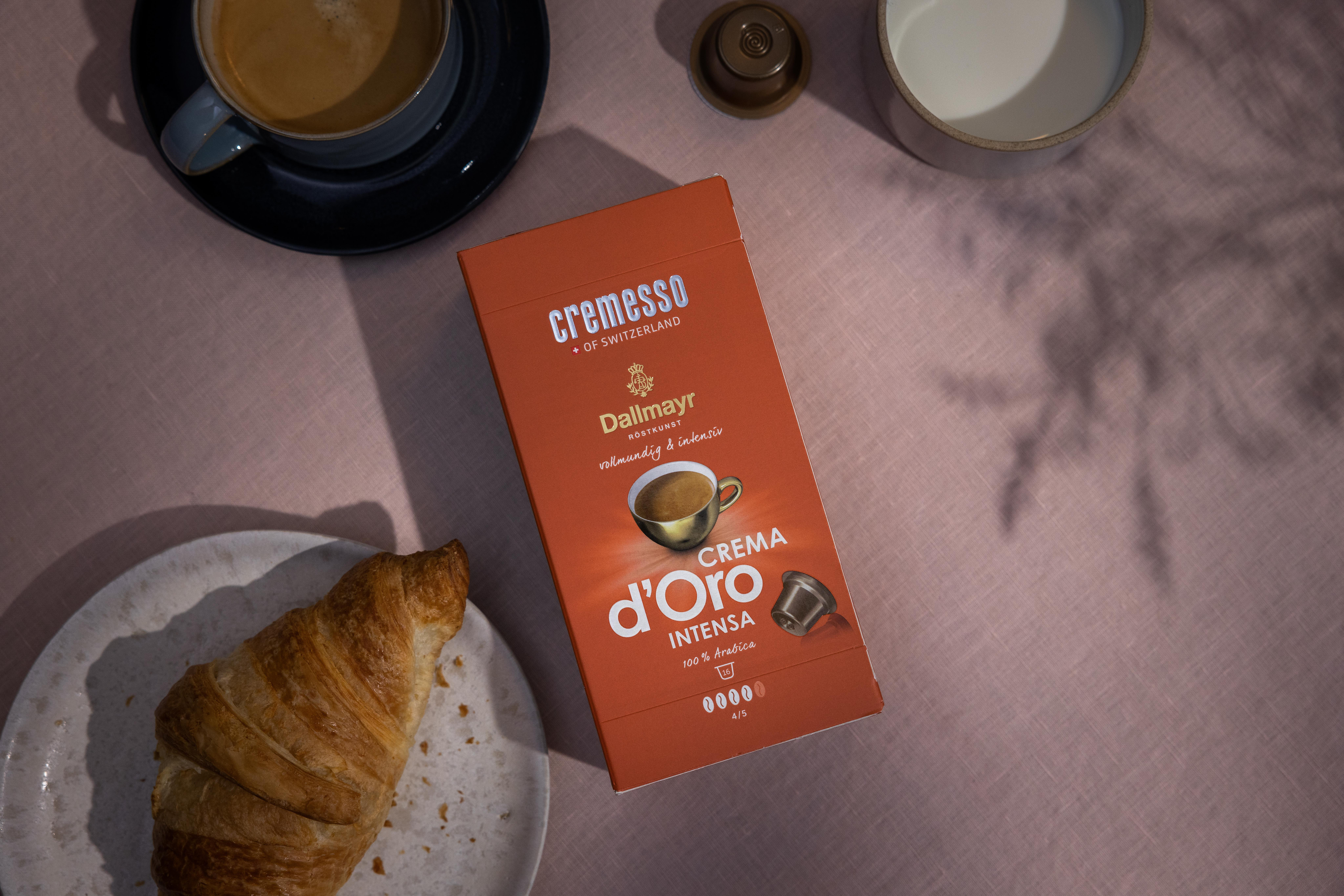 Kaffee, Croissant und Kaffeekapseln auf rosa Oberfläche. Schatten vorhanden.