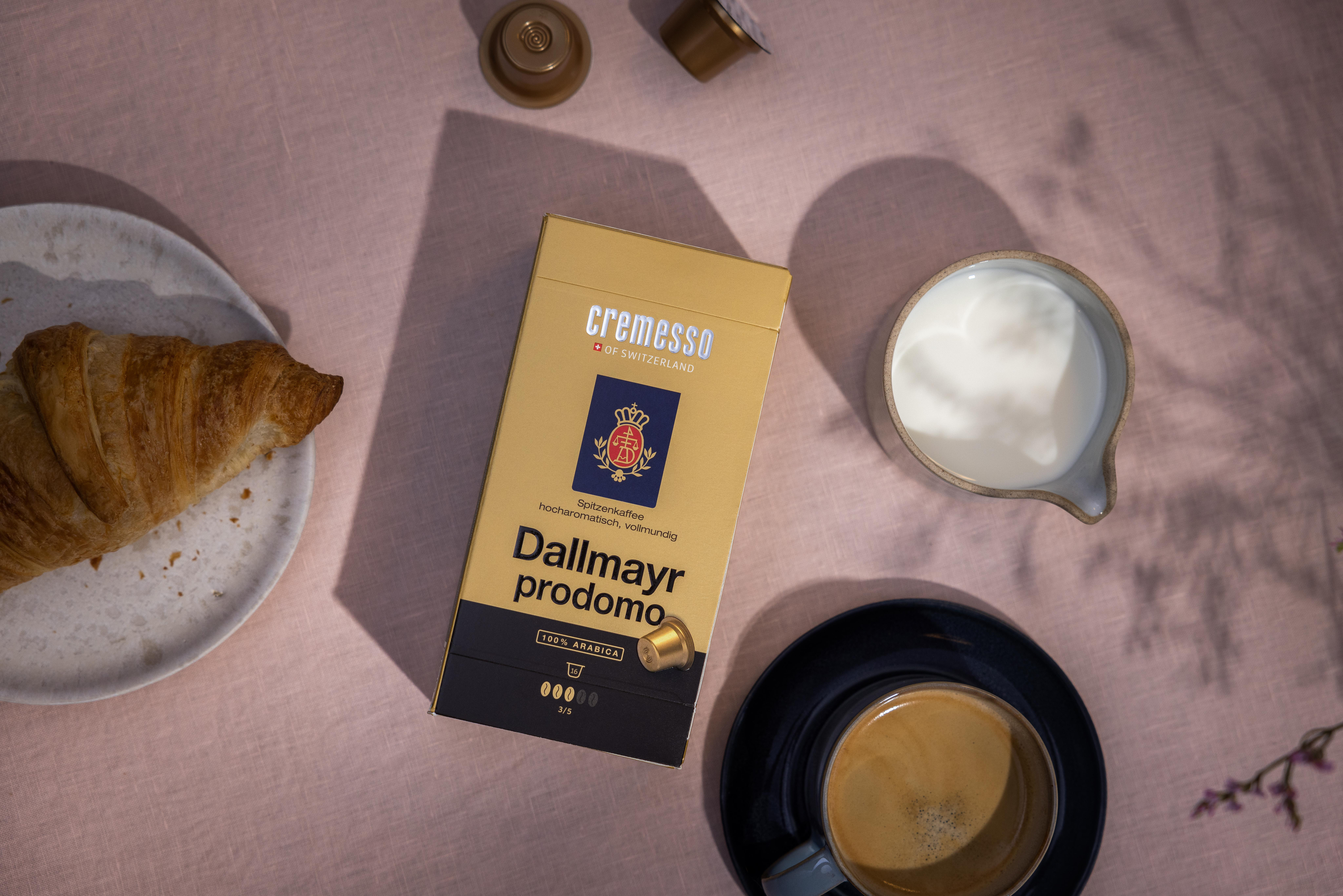 Goldene Kaffeebox mit Croissant, Kaffeetasse, Sahne und Kaffeepads.