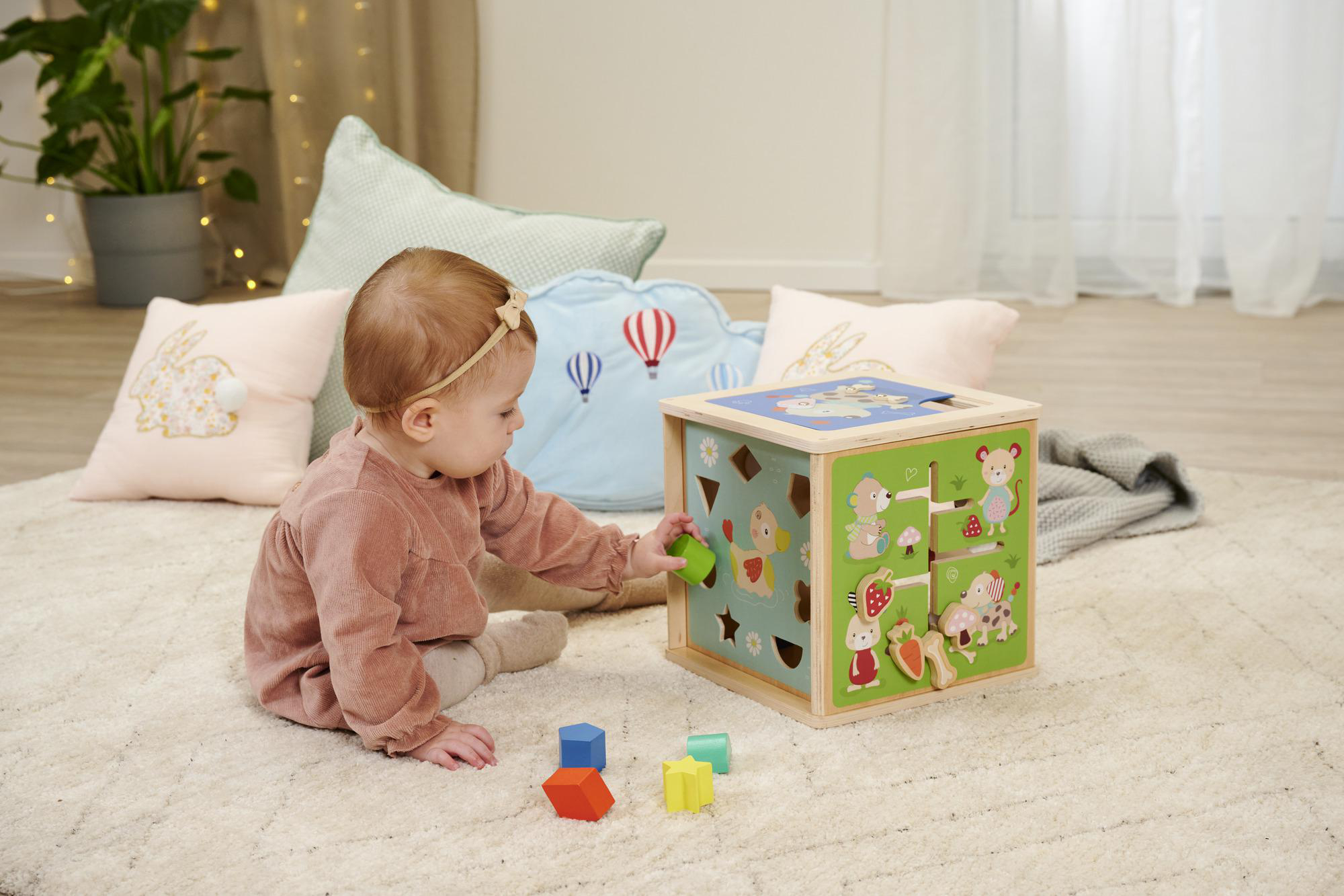 Kleines Kind spielt mit einem bunten Holzspielzeug auf dem Boden.
