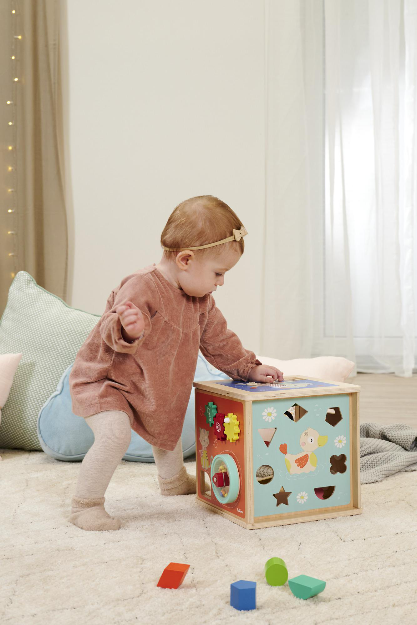Ein Baby steht mit einem hölzernen Würfelspielzeug mit verschiedenen Formen und Farben.
