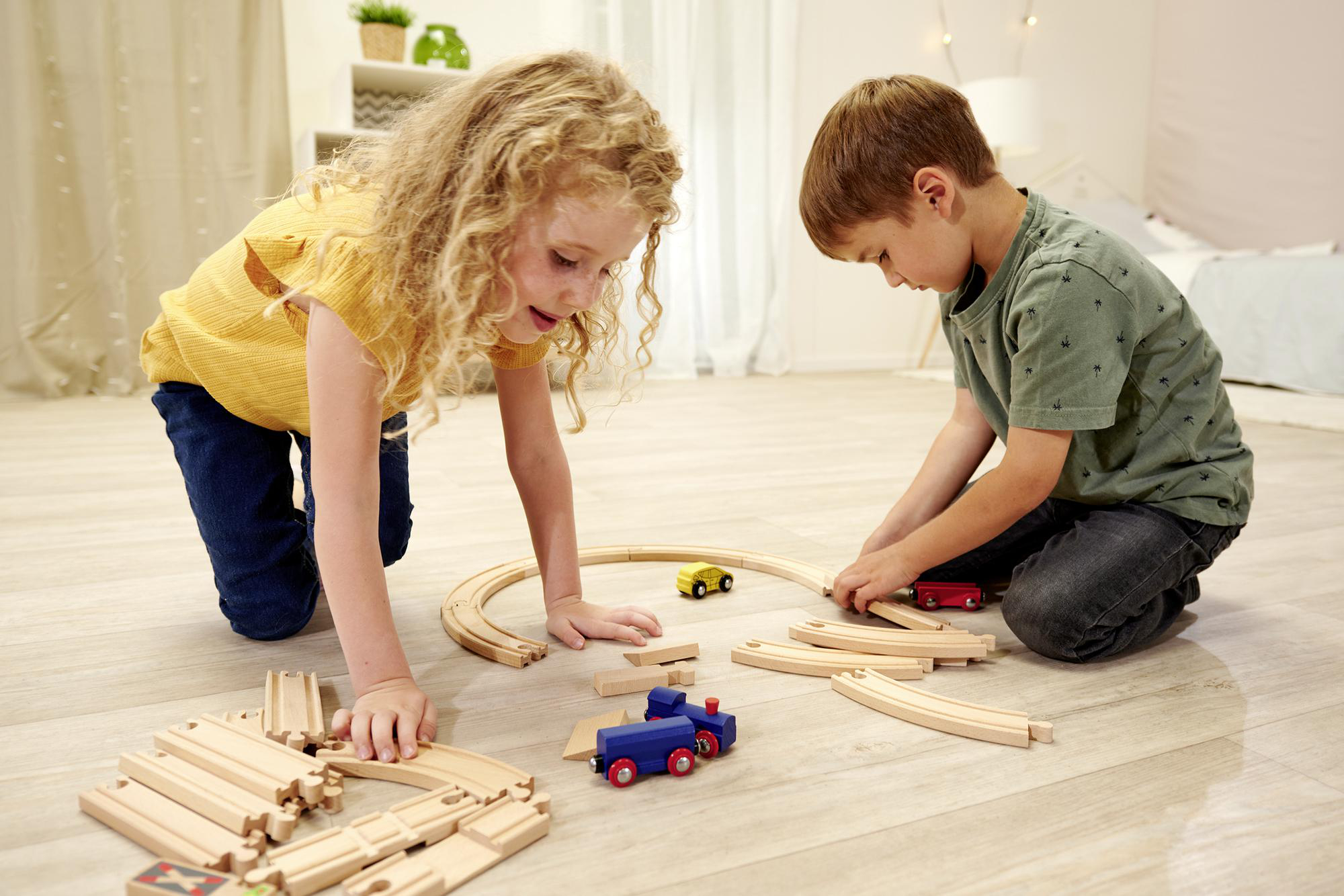 Zwei Kinder spielen mit einem Holzeisenbahn-Set auf dem Boden. Holzschienen und Spielzeug.