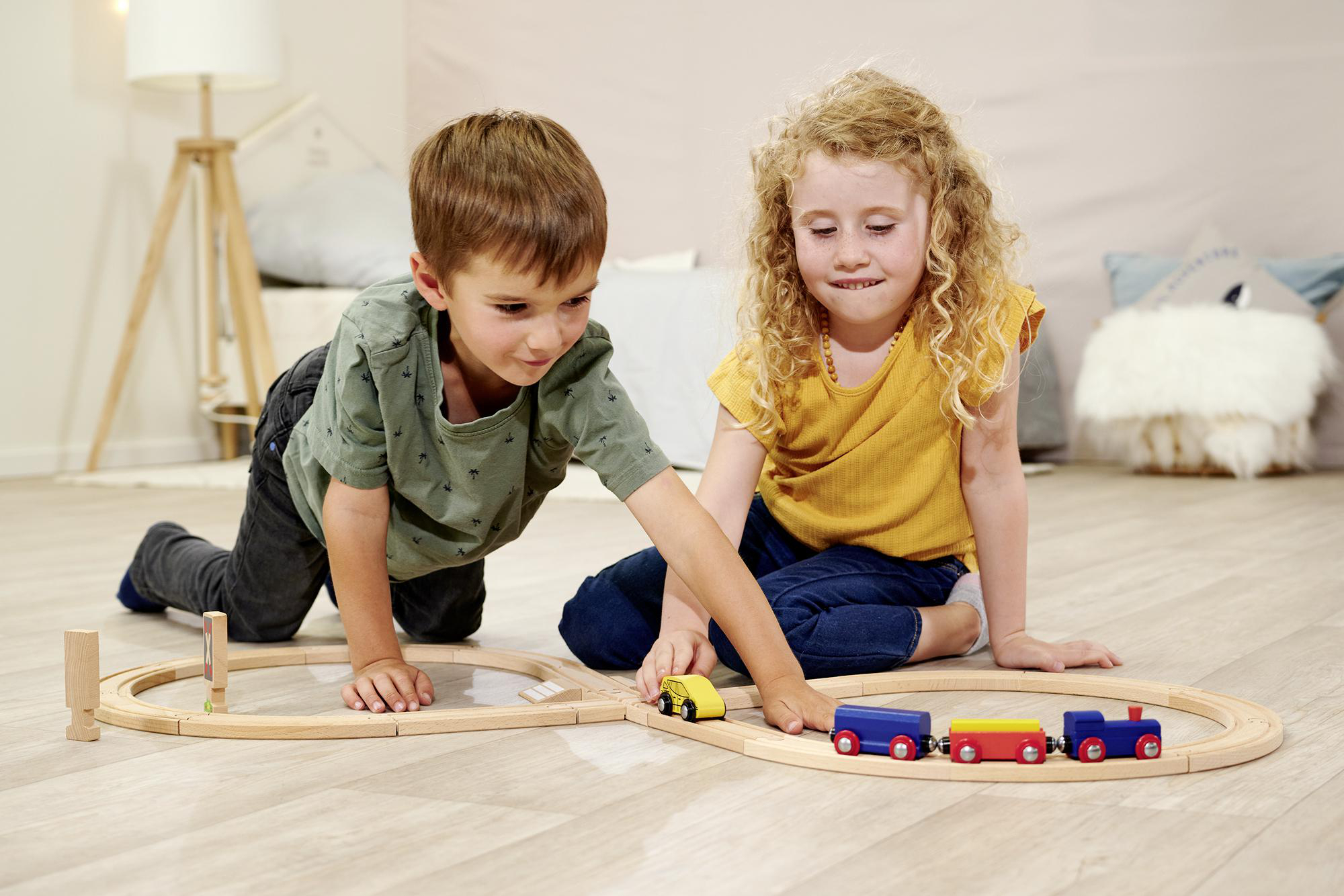 Zwei Kinder spielen auf einem Holzboden mit einer Holzeisenbahn.