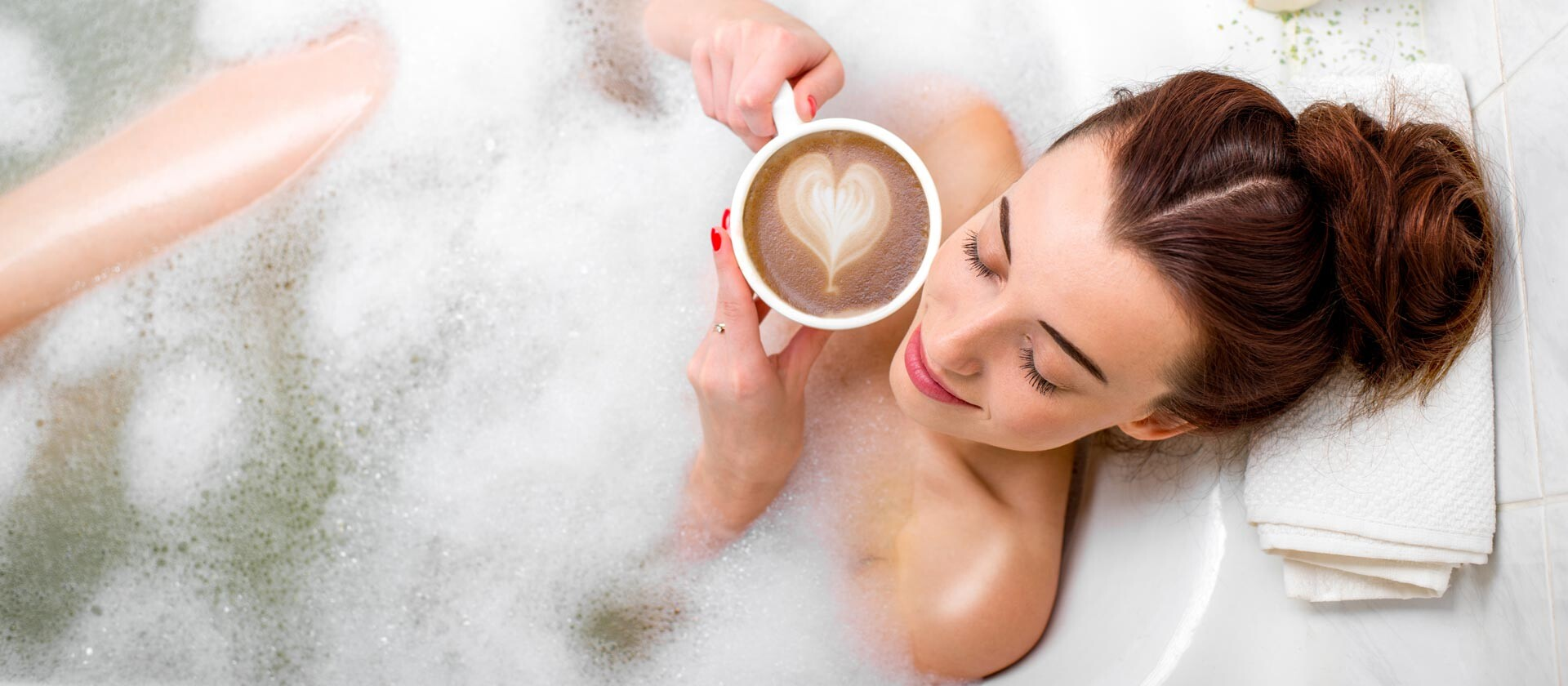 Nő a fürdőkádban, buborékokkal, szív alakú habbal a kávéscsészében. Relaxál.