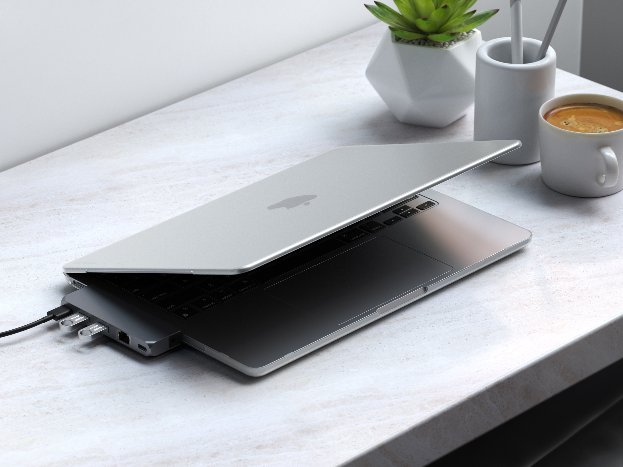 Laptop aperto con hub USB e tazza di caffè su una superficie in marmo.
