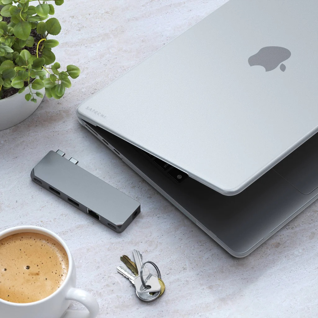 Laptop con hub, tazza di caffè, chiavi e pianta su superficie in marmo.