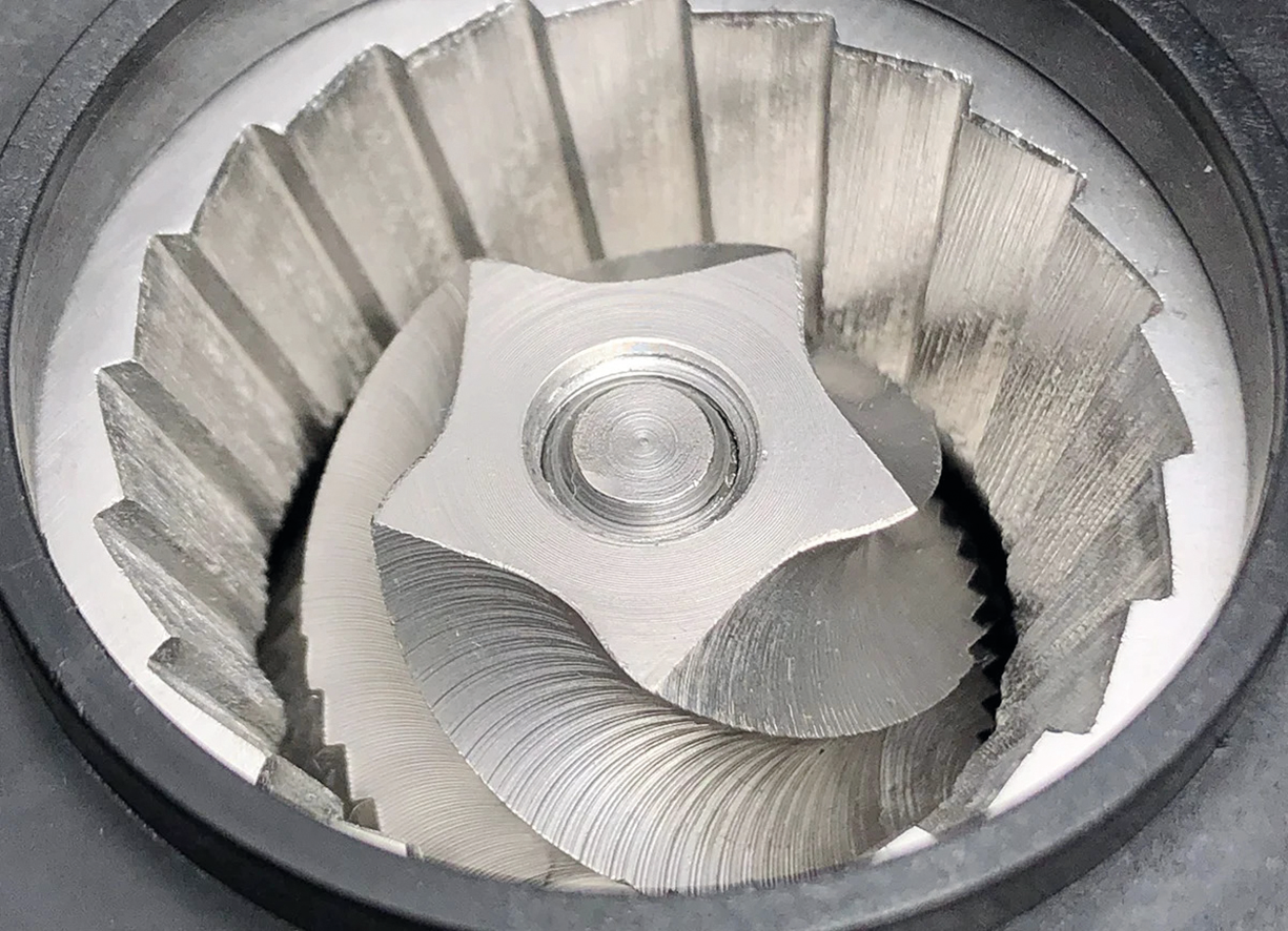 Primo piano del meccanismo di macinazione di un macinacaffè. Le lame sono argentate e angolari, a spirale.