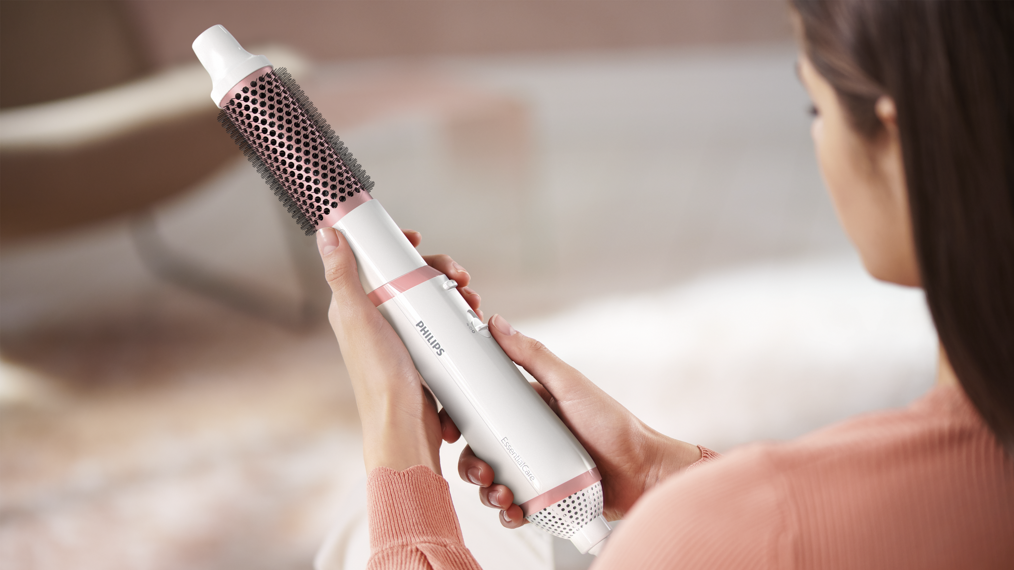 Una persona sosteniendo un cepillo para peinar el cabello blanco y rosa. El cepillo es cilíndrico.