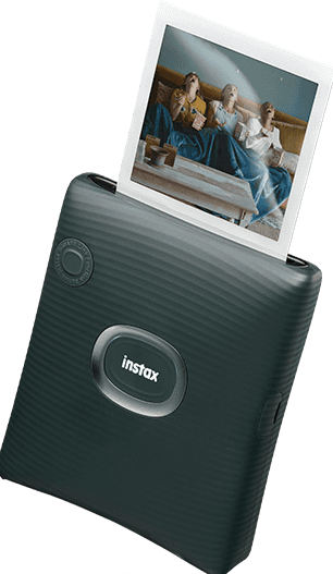 Stampante Instax grigio scuro che stampa una foto. La foto mostra tre persone che ridono mentre guardano qualcosa.