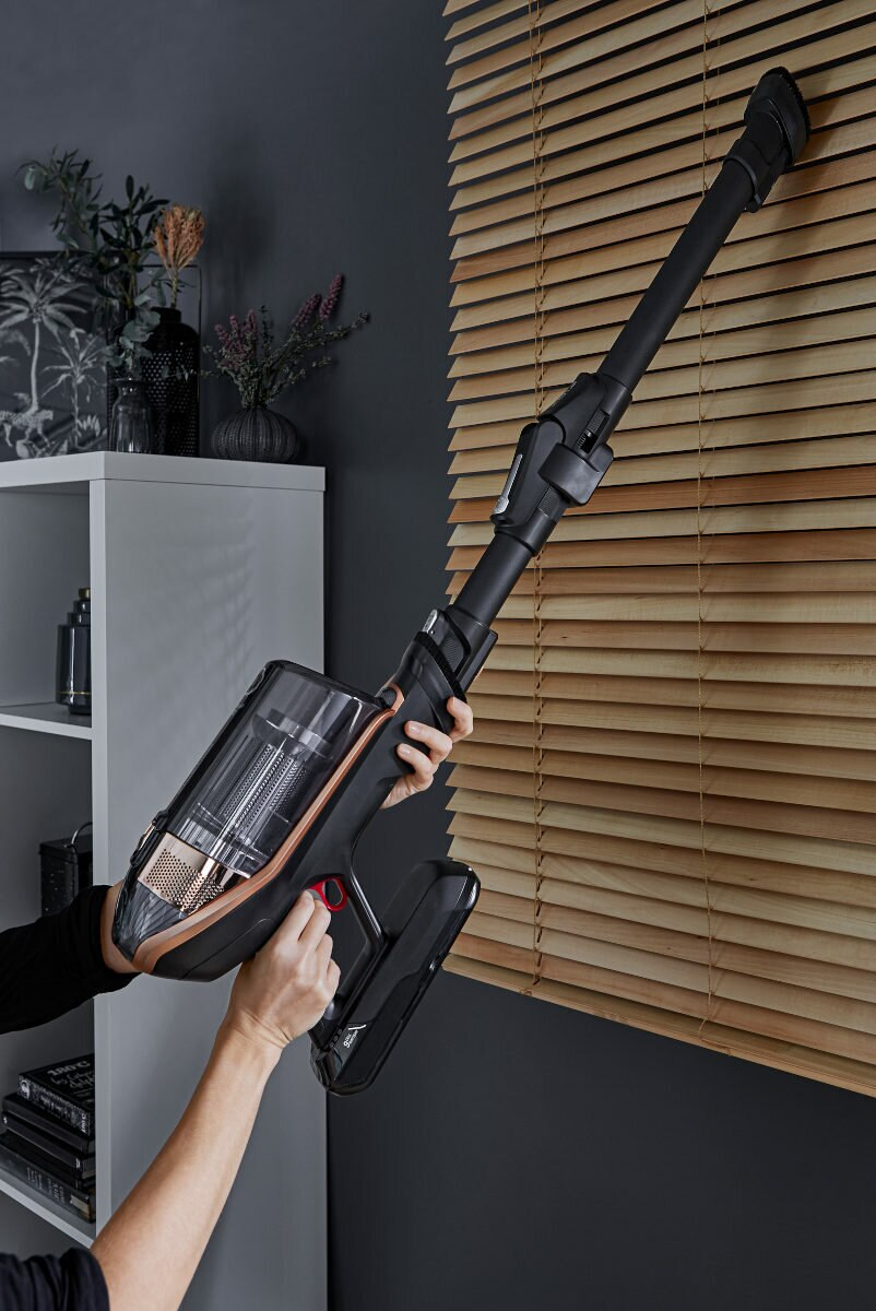 Osoba używająca czarno-miedzianego odkurzacza bezprzewodowego.