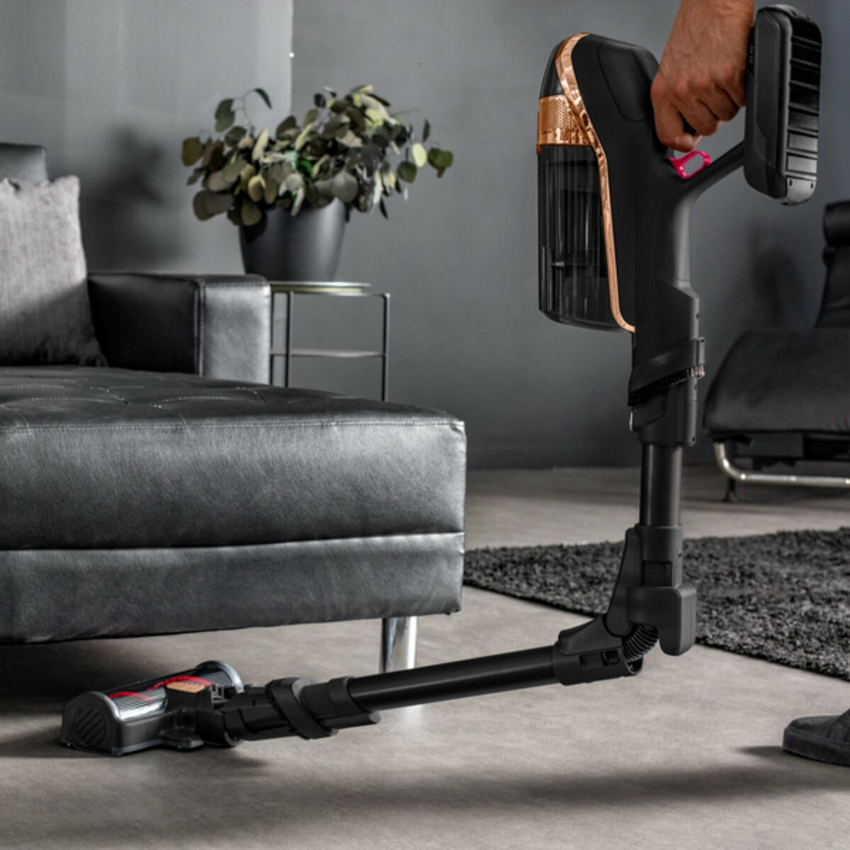 Czarny i złoty bezprzewodowy odkurzacz trzymany i używany na czarnym dywanie.