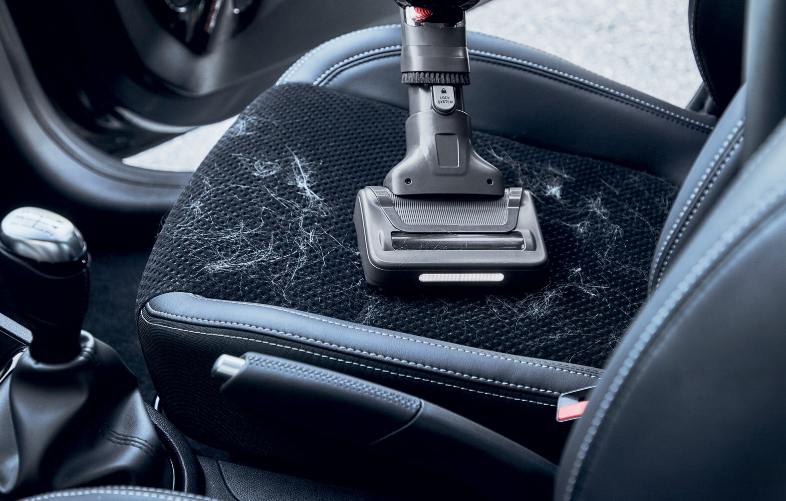 Odkurzacz z końcówką szczotkową czyszczący fotel samochodowy. Siedzisko pokryte jest sierścią zwierząt.