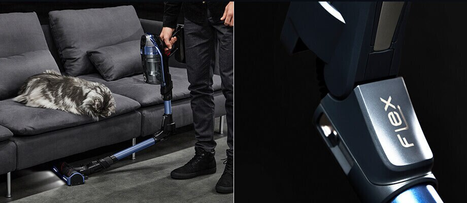 Osoba używająca niebiesko-czarnego odkurzacza bezprzewodowego na dywanie obok sofy z kotem.