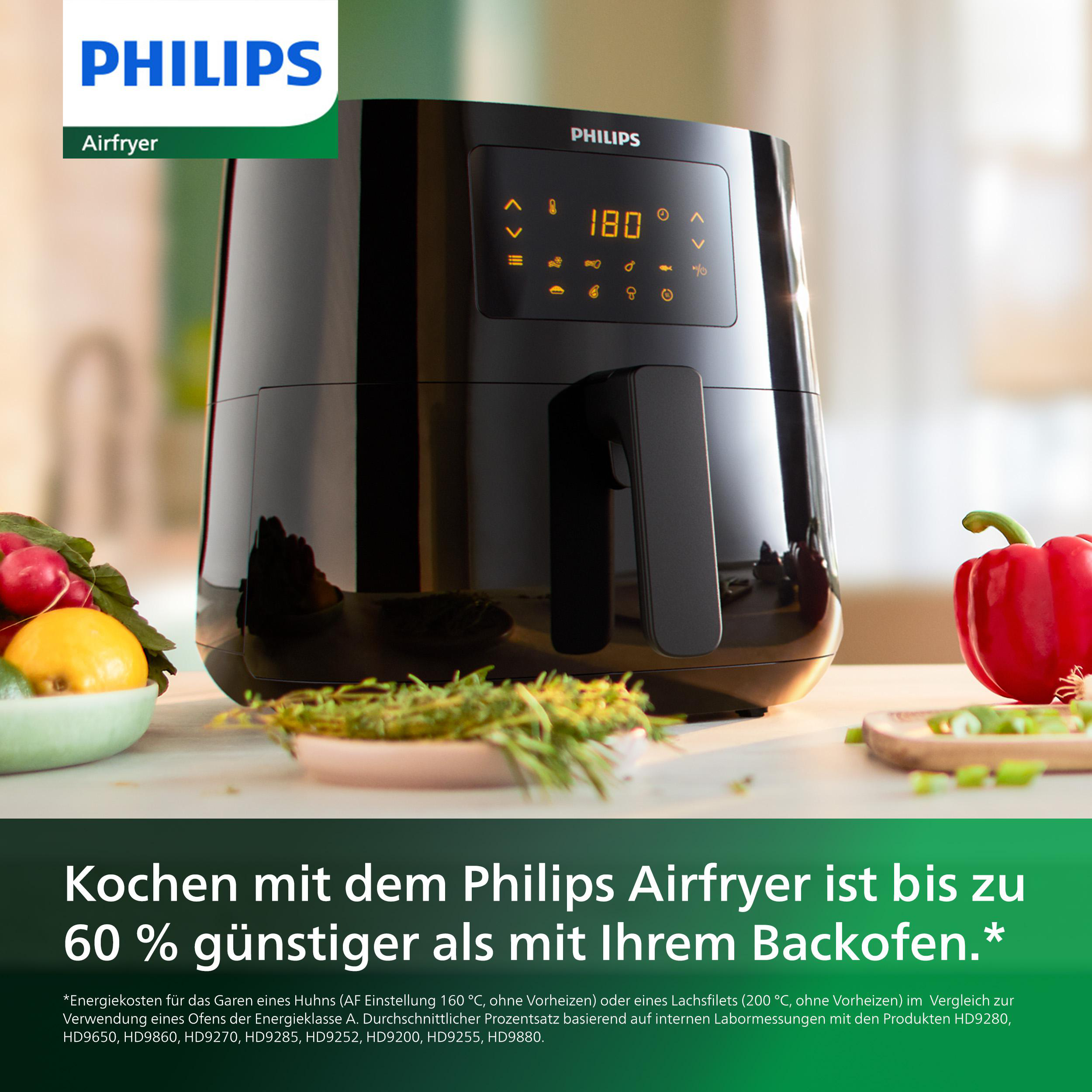 Schwarze Philips Airfryer mit Griff, grüne Oberfläche und Text darauf. Rote Paprika und andere Lebensmittel.