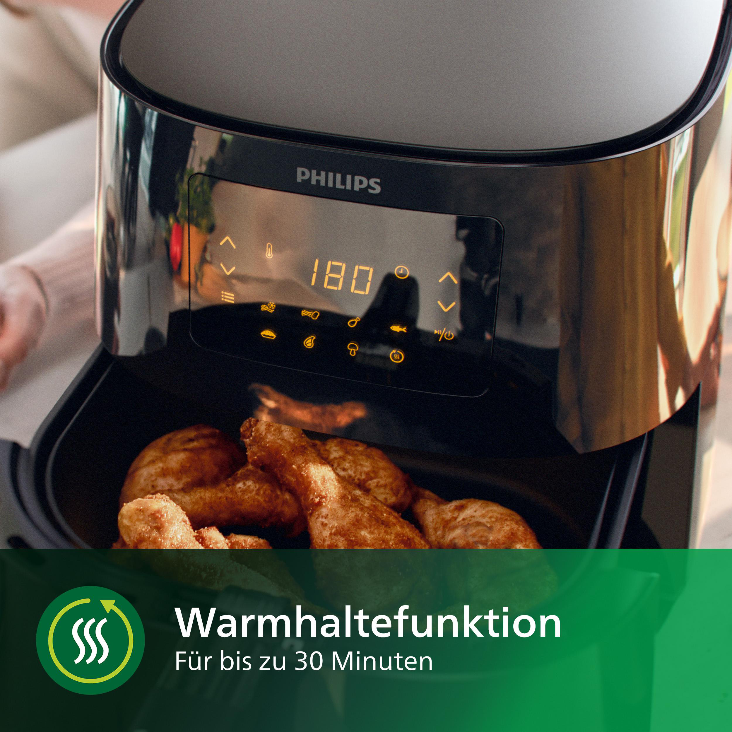 Schwarze Heißluftfritteuse mit Hähnchenschenkeln. Digitalanzeige zeigt 180. Grüner Hintergrund.