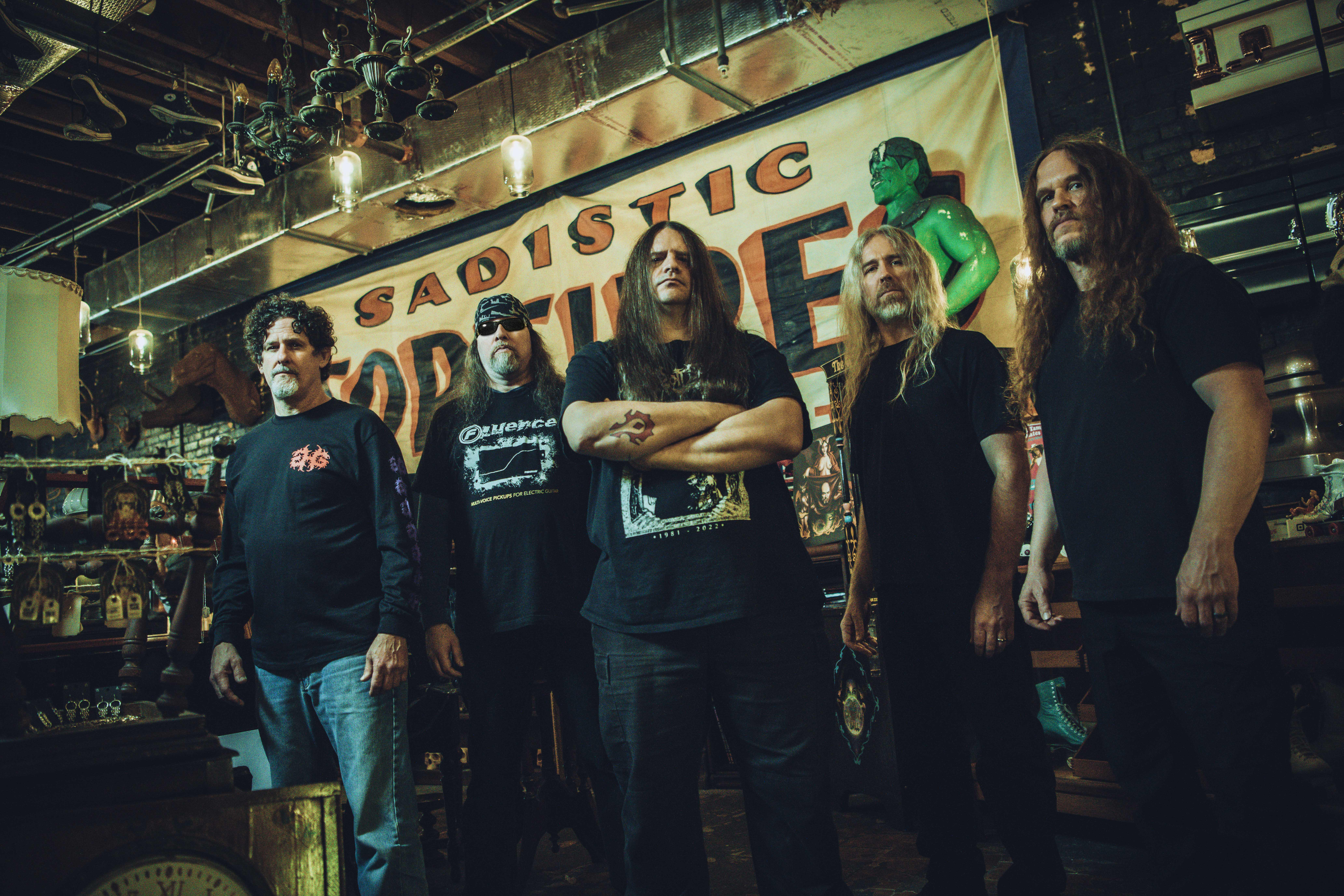 Eine Band von fünf Männern steht in einem überfüllten Raum. Es gibt ein Banner mit der Aufschrift "SADISTIC TORTURES".