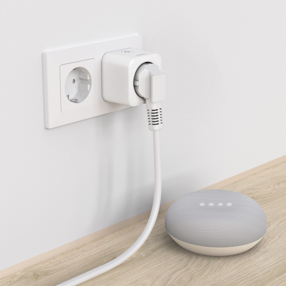 Weiße Steckdose mit eingestecktem Smart-Stecker. Ein Google Home Mini ist in der Nähe. Auf einem Holztisch.