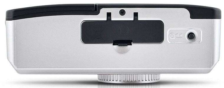 Back of a silver camera. There is a battery compartment, a charging port, and a button.